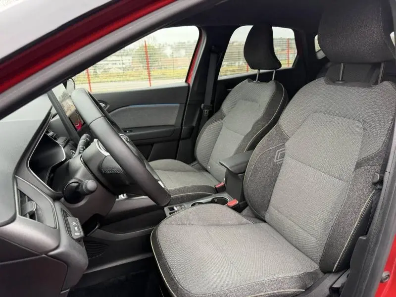 Vue intérieure côté gauche du Renault Captur 2025 Rouge Flamme, montrant les sièges avant gris et le volant.