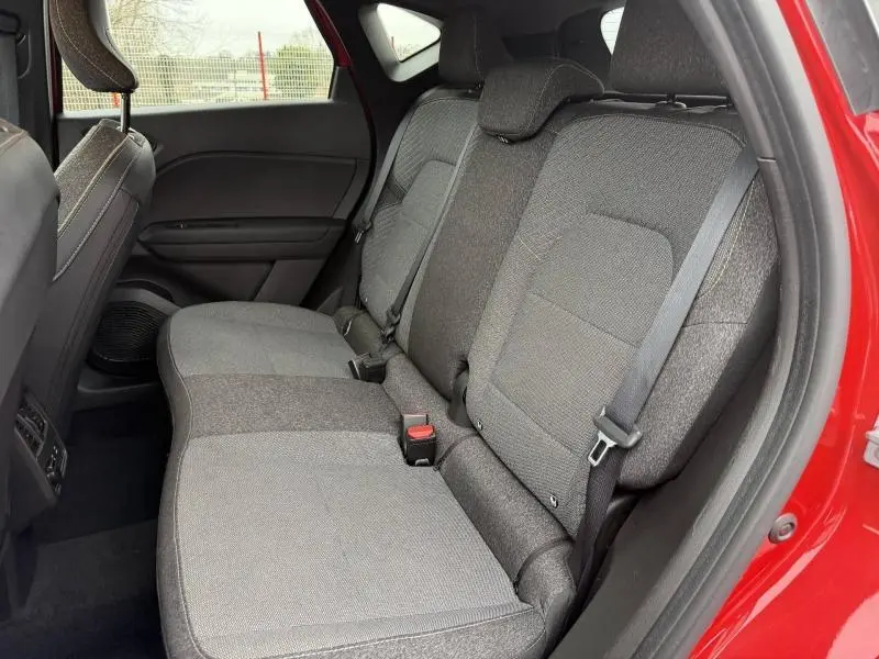 Vue intérieure côté arrière droit du Renault Captur 2025 rouge flamme, montrant la banquette arrière en tissu gris.