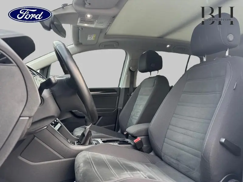 Vue intérieure côté conducteur du Volkswagen Touran 1.5 TSI 2021, sièges tissu gris et toit ouvrant panoramique visible.