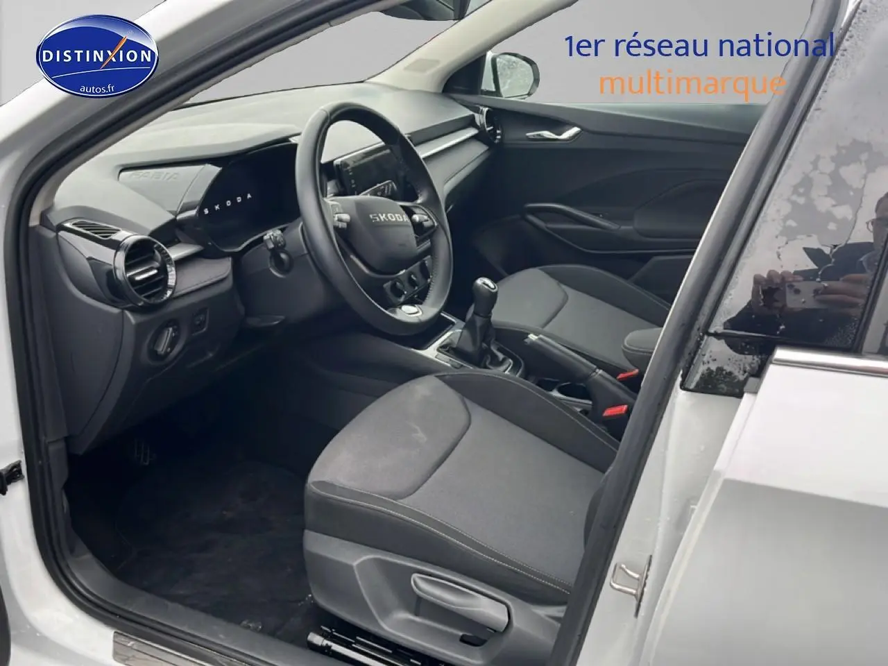 Vue intérieure côté conducteur d'une Skoda Fabia blanche 2025, avec volant cuir et boîte manuelle visible.