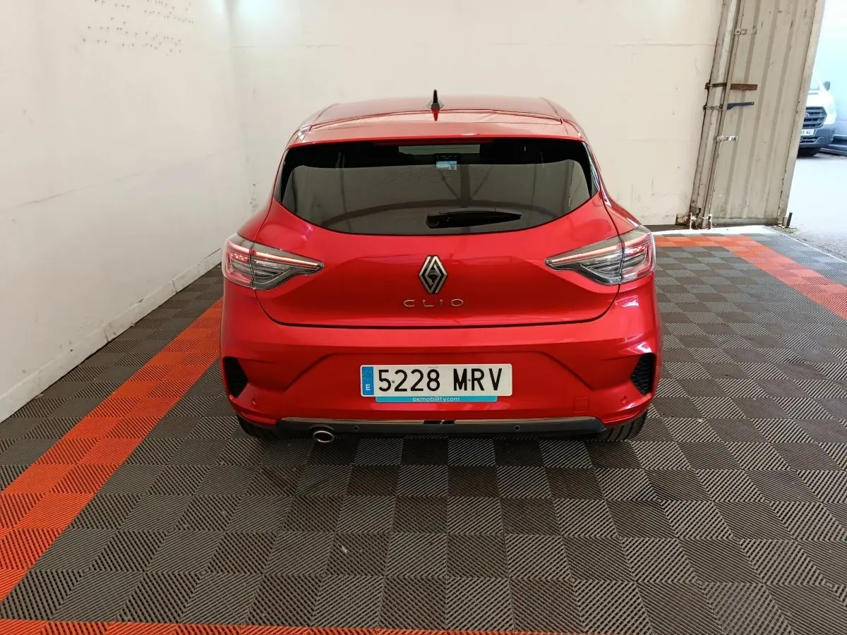 Vue arrière d'une Renault Clio rouge 2024 garée en intérieur avec feux arrière LED et échappement sport visible.