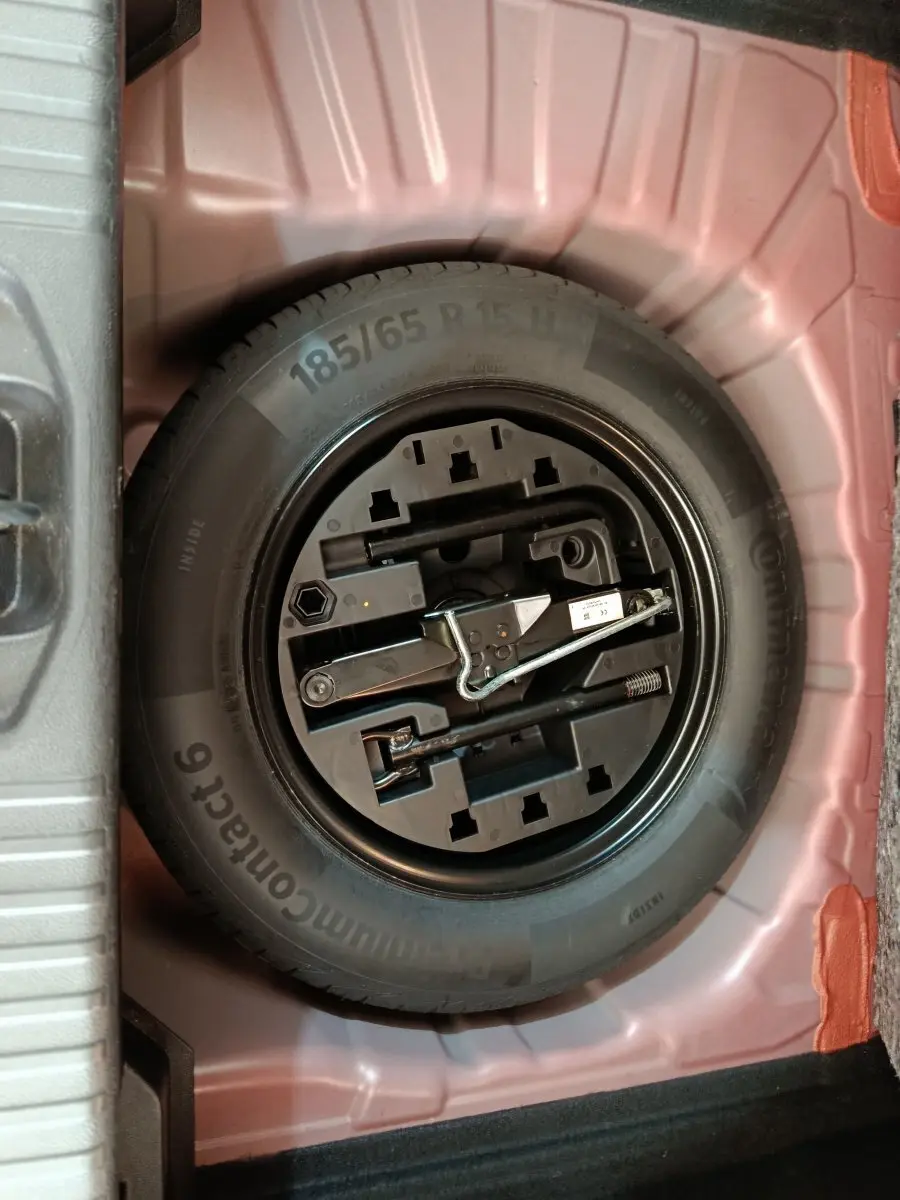 Vue plongeante sur la roue de secours noire et ses outils dans le coffre rouge de la Renault Clio Techno TCe 90 2024.
