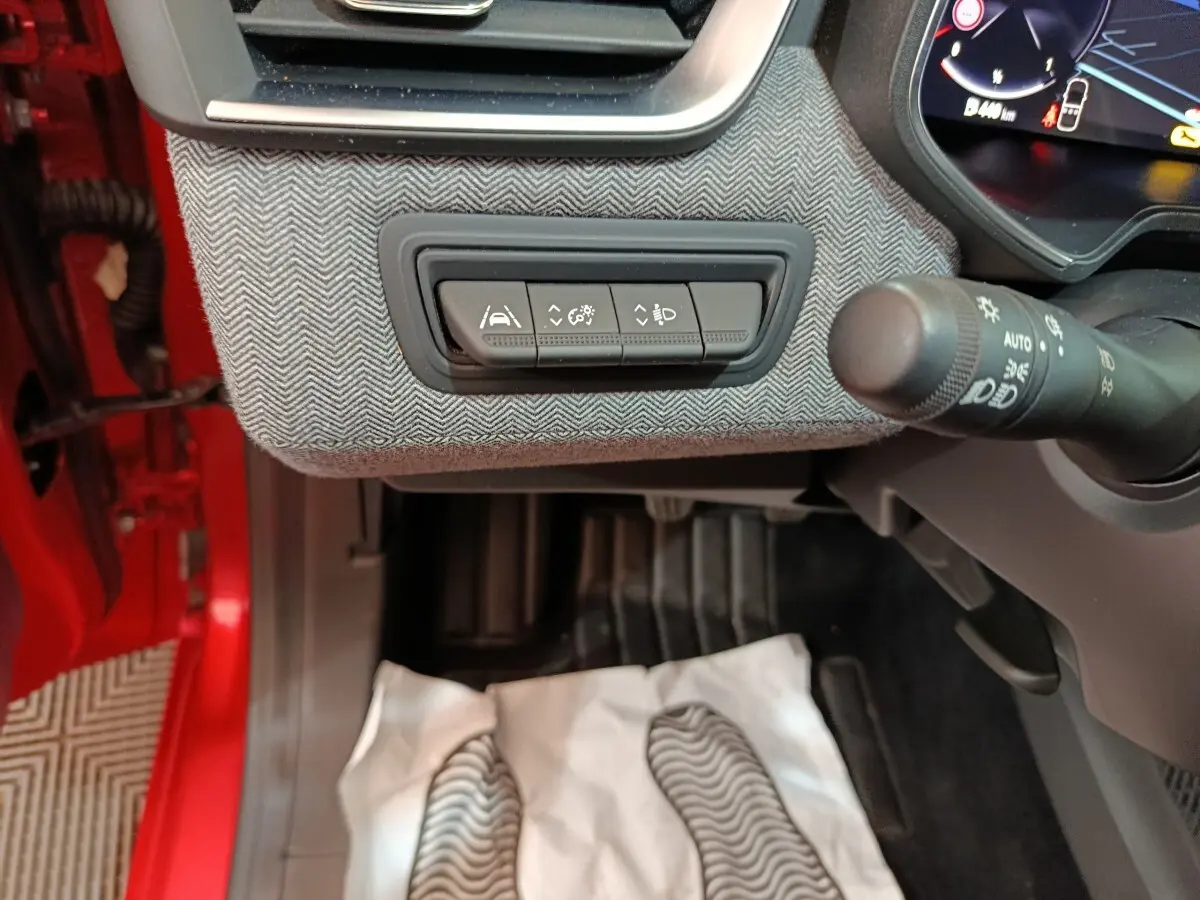 Vue intérieure côté conducteur de la Renault Clio Techno TCe 90 rouge 2024, avec commandes d’aide à la conduite et volant partiel.