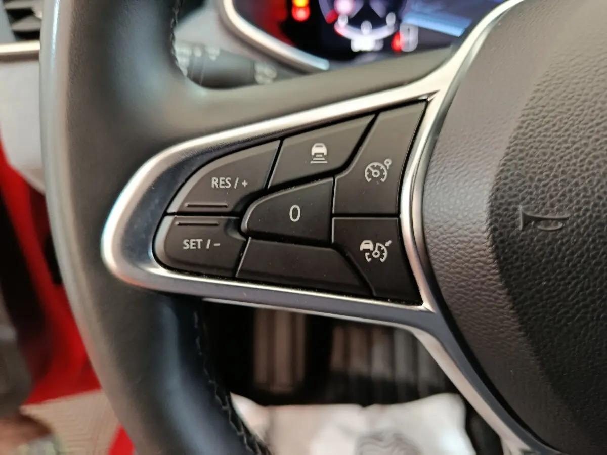 Gros plan sur les commandes du régulateur de vitesse au volant cuir d’une Renault Clio Techno rouge 2024.