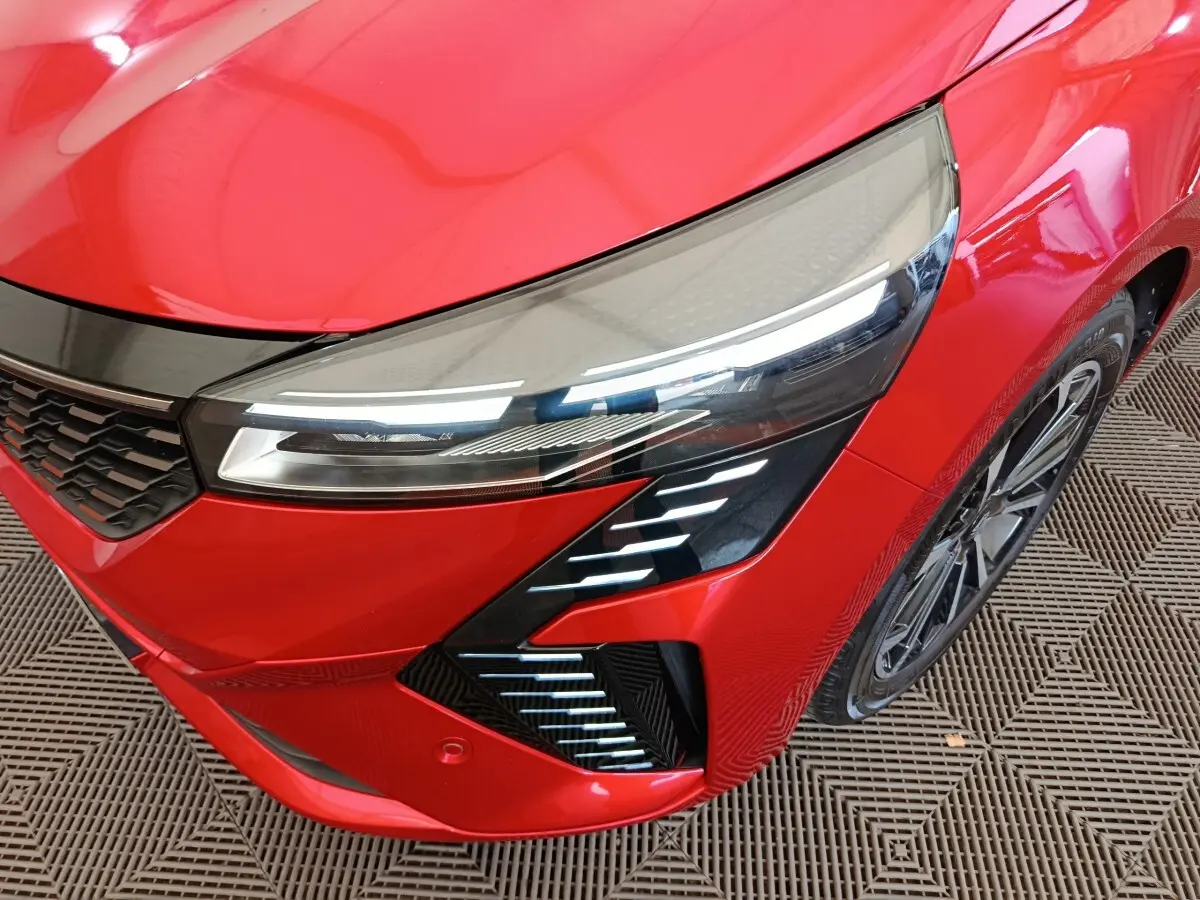 Gros plan sur l'avant droit de la Renault Clio Techno TCe 90 rouge, mettant en valeur son phare LED et la calandre noire.