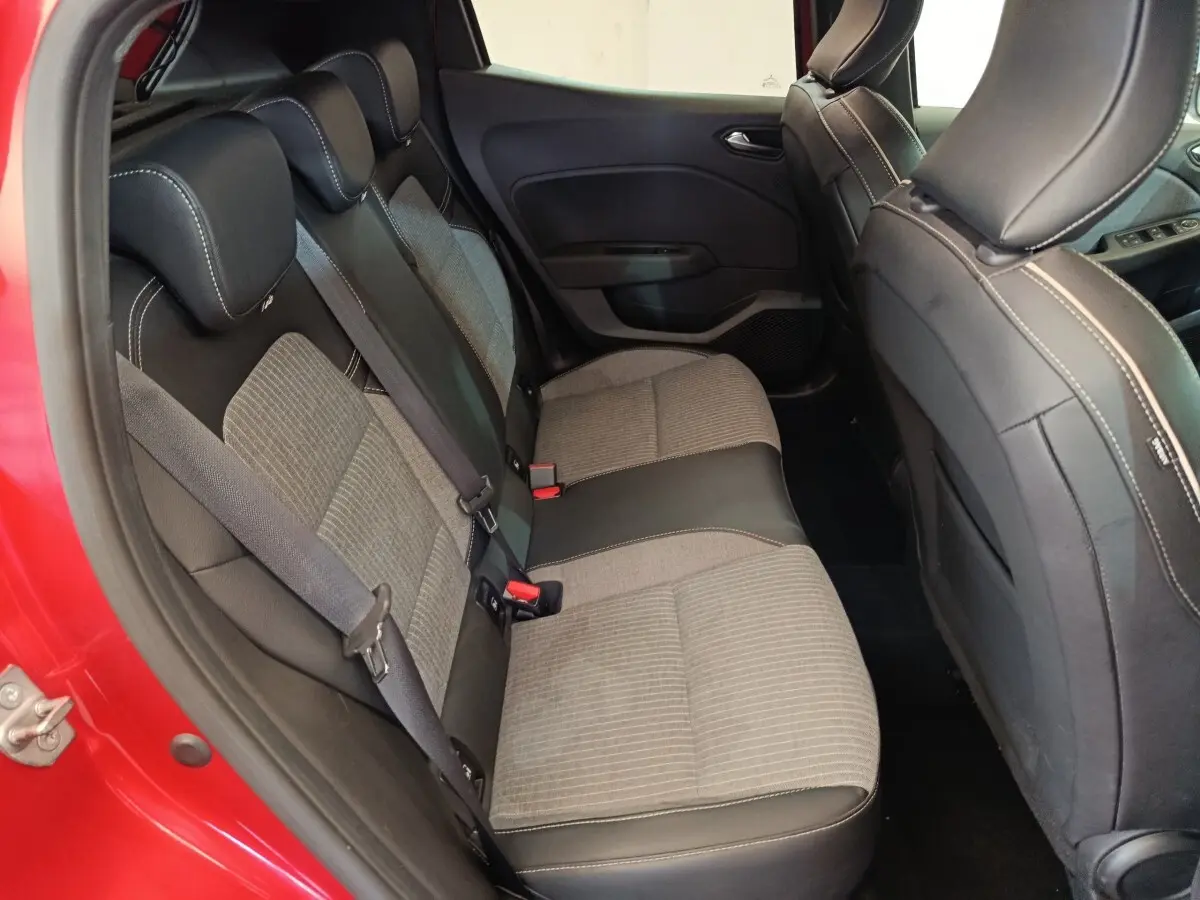 Vue intérieure côté arrière gauche de la Renault Clio rouge 2024, mettant en valeur la banquette arrière bicolore tissu et cuir.