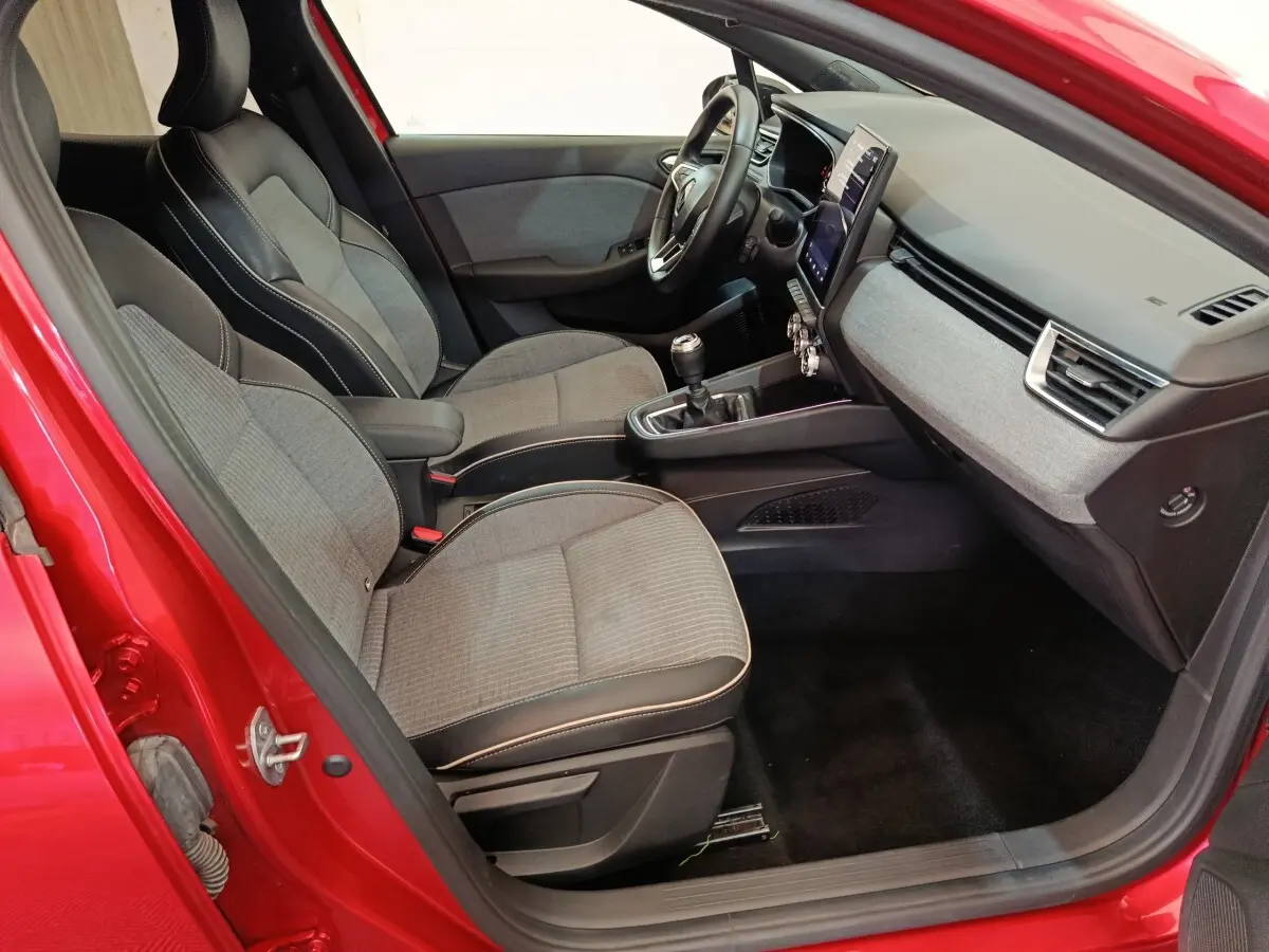 Vue intérieure côté conducteur de la Renault Clio Techno TCe 90 rouge 2024, avec sièges tissu et tableau de bord moderne.