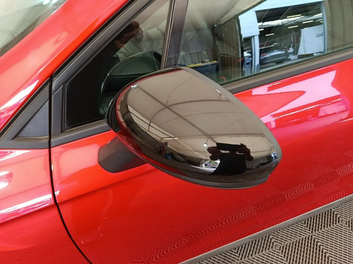 Gros plan sur le rétroviseur côté conducteur noir brillant d'une Renault Clio Techno TCe 90 rouge 2024.