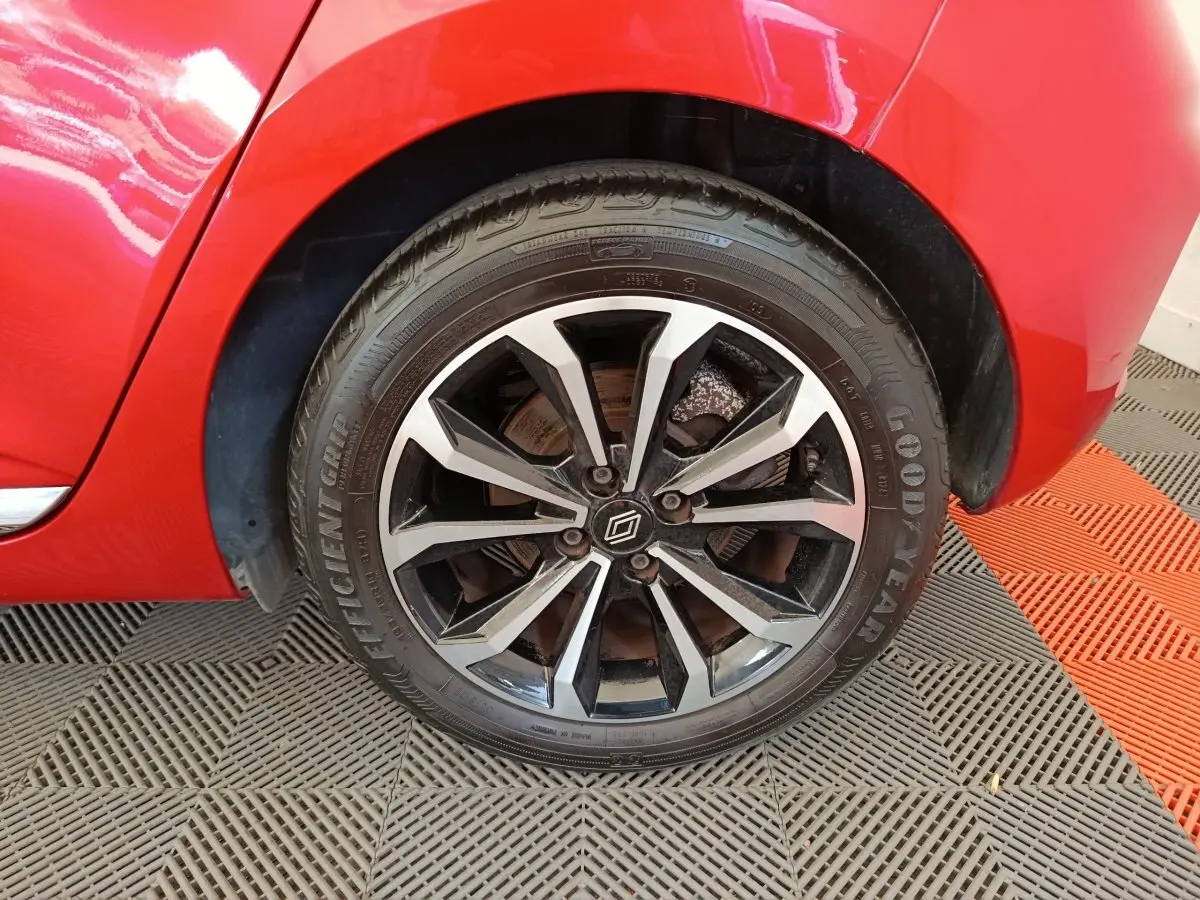 Gros plan sur la roue avant droite d'une Renault Clio rouge 2024 avec jante alliage bicolore et logo Renault au centre.