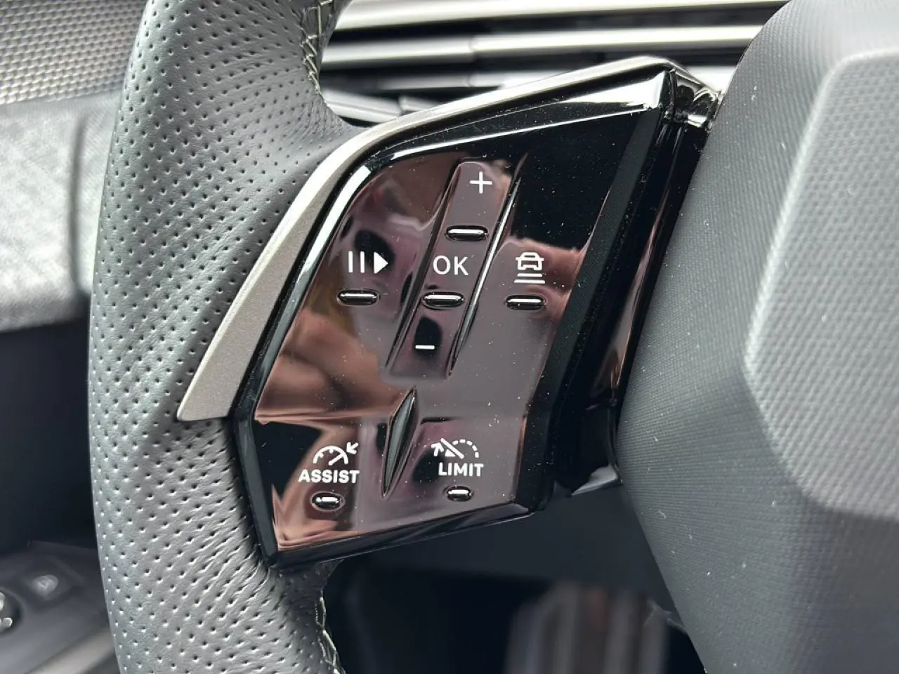 Gros plan sur les commandes gauche du volant noir perforé du Peugeot 3008 GT 2026 avec boutons de régulateur et limiteur.