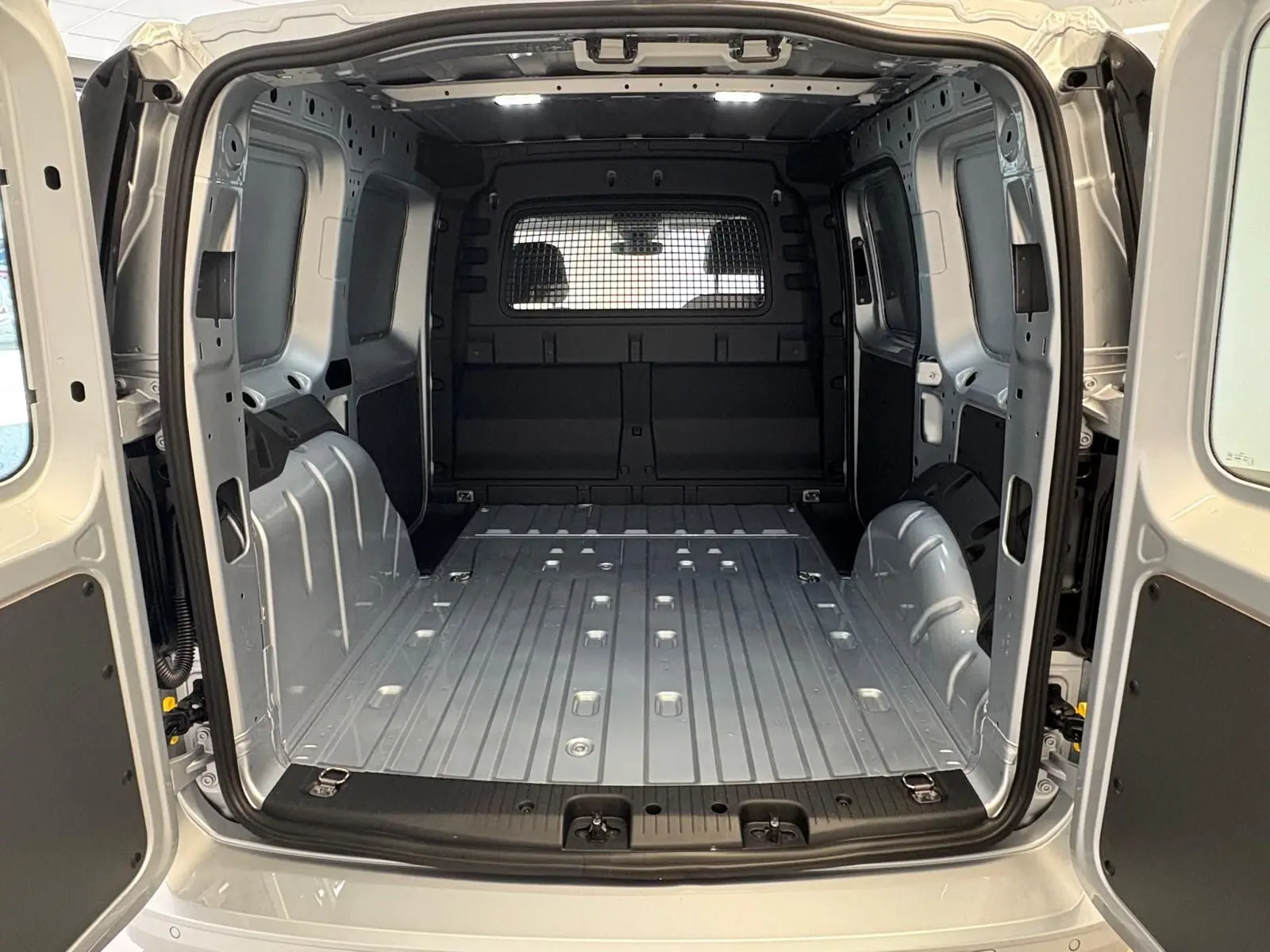 Vue arrière du Volkswagen Caddy 2025 gris argent, montrant l'espace de chargement vide et la cloison métallique séparant la cabine.