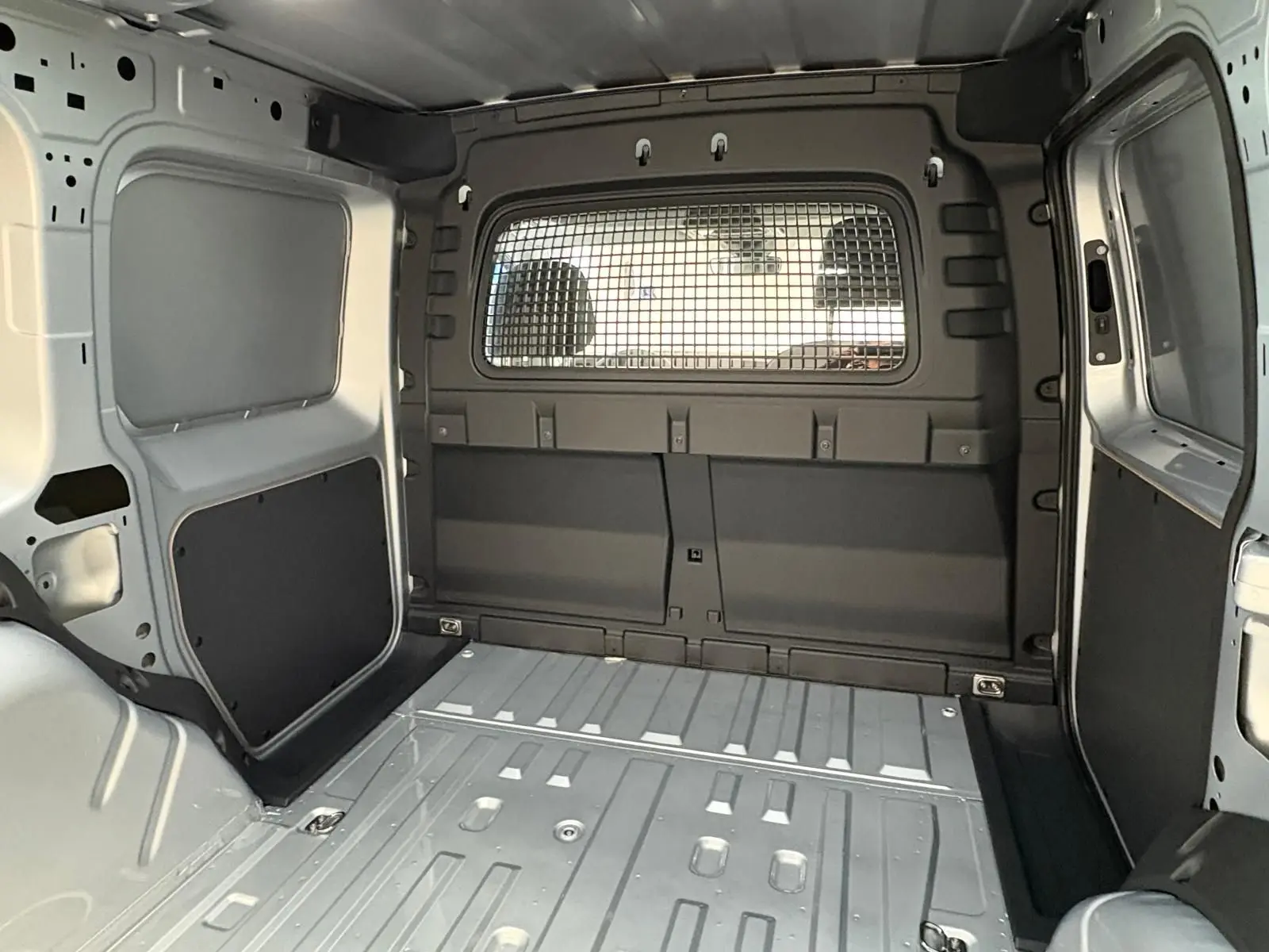 Vue intérieure de la zone de chargement du Volkswagen Caddy 2025 gris argent avec cloison métallique séparant l'habitacle.