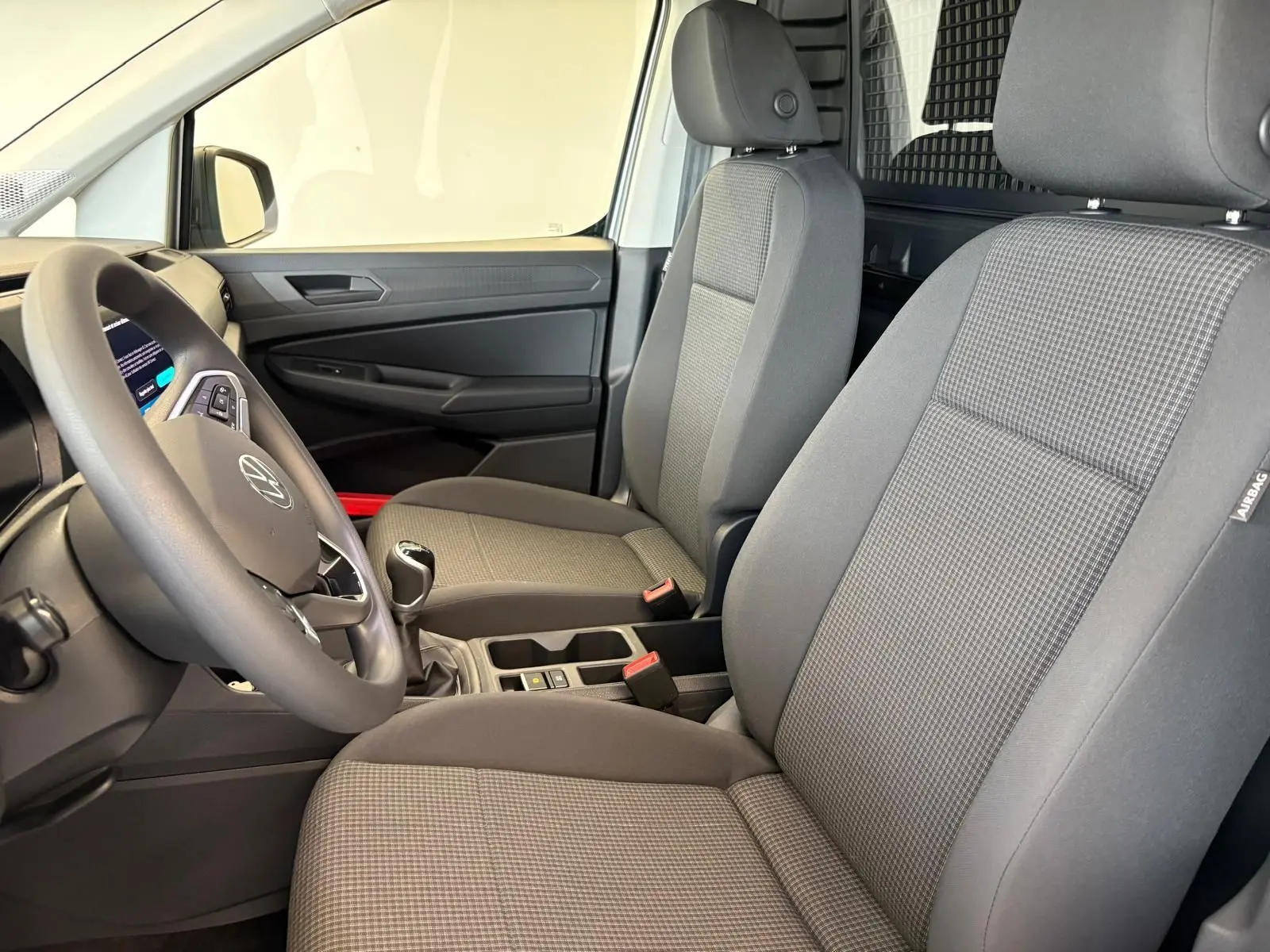 Intérieur du Volkswagen Caddy 2025 en gris argent, vue côté conducteur montrant sièges et volant avec levier de vitesse manuel.