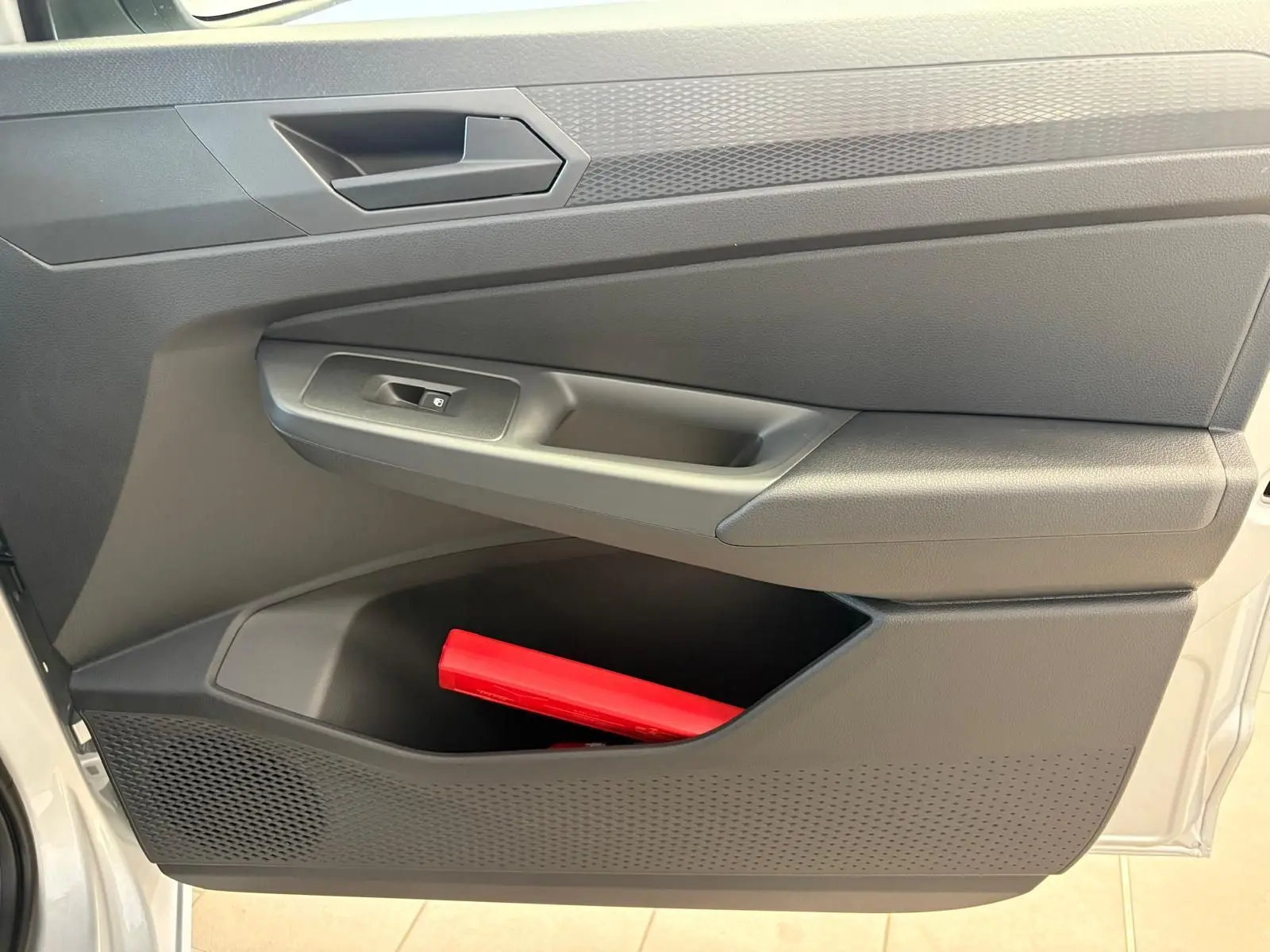 Intérieur de la porte côté gauche d'un Volkswagen Caddy gris argent 2025 avec rangement et triangle de signalisation rouge visible.