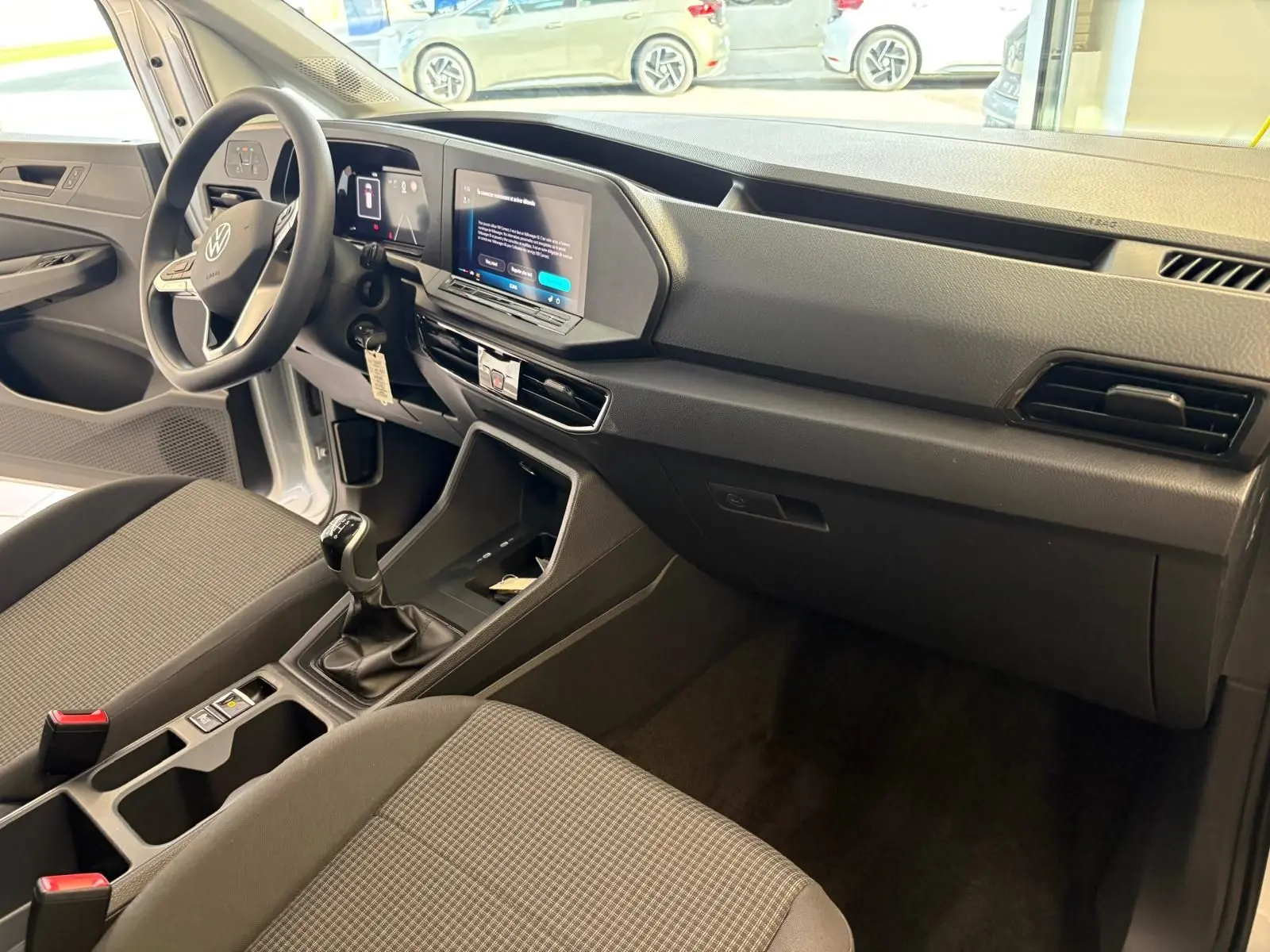Intérieur du Volkswagen Caddy 2025 gris argent, vue côté conducteur sur le tableau de bord et la boîte manuelle.