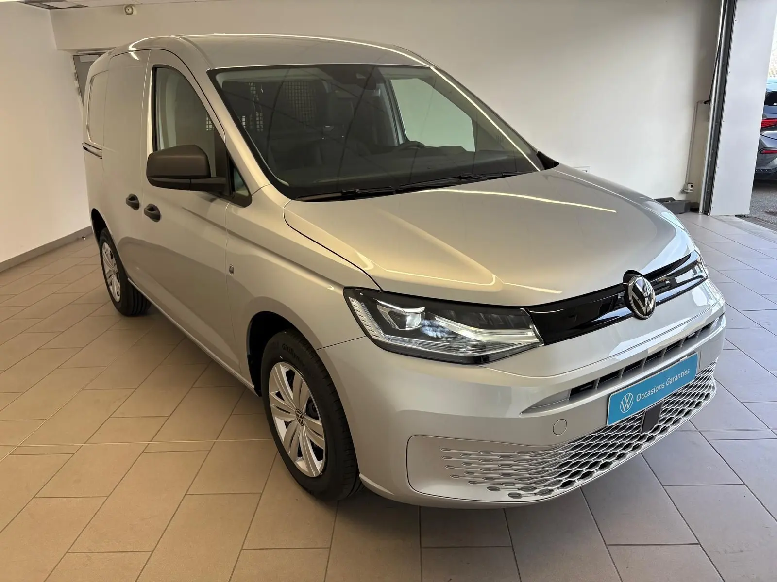 Vue 3/4 avant droite du Volkswagen Caddy 2025 gris argent avec calandre noire et phares modernes.