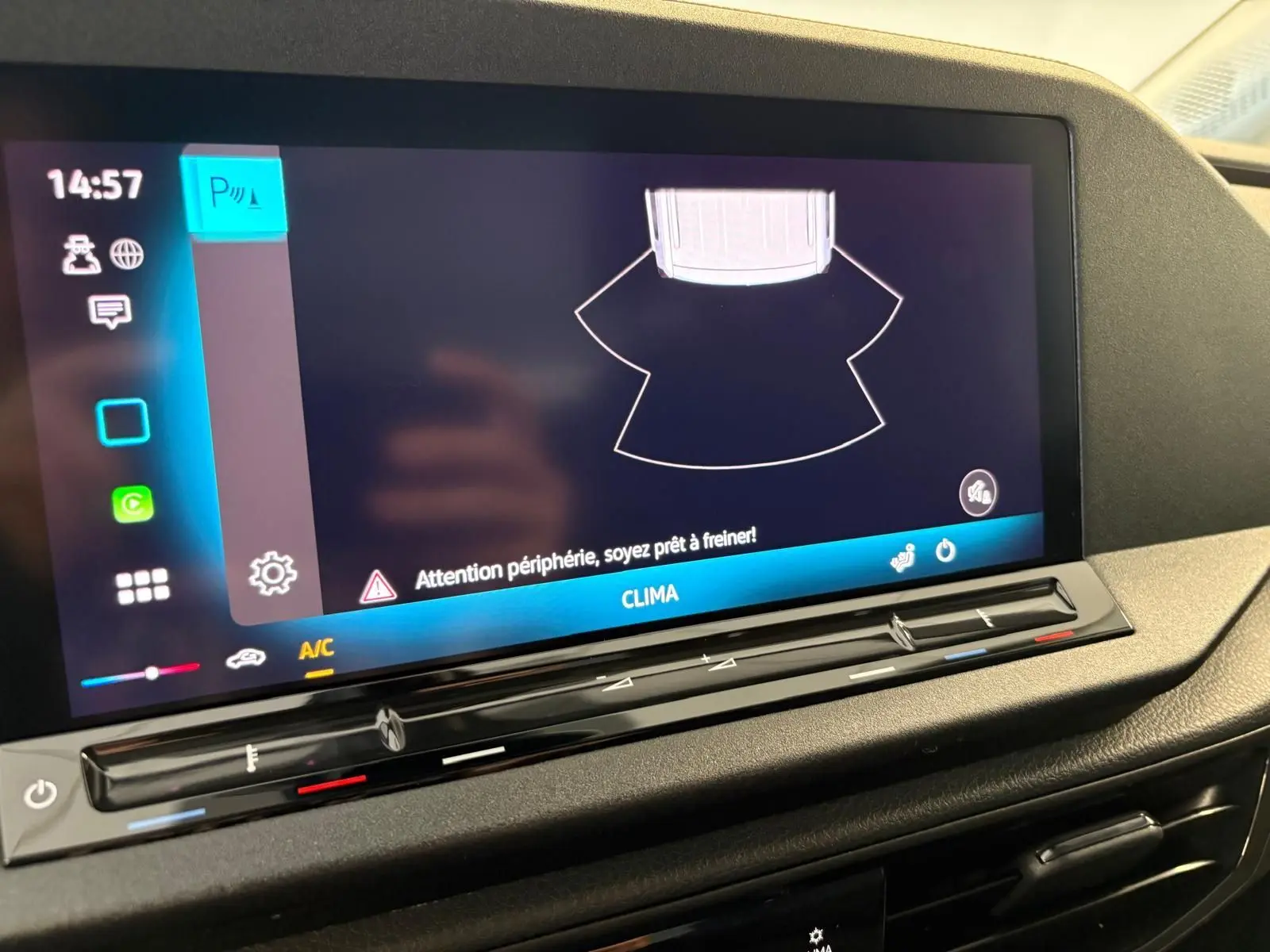 Écran tactile du tableau de bord du Volkswagen Caddy 2025 gris argent, affichant l'alerte de périphérie et commandes climatisation.