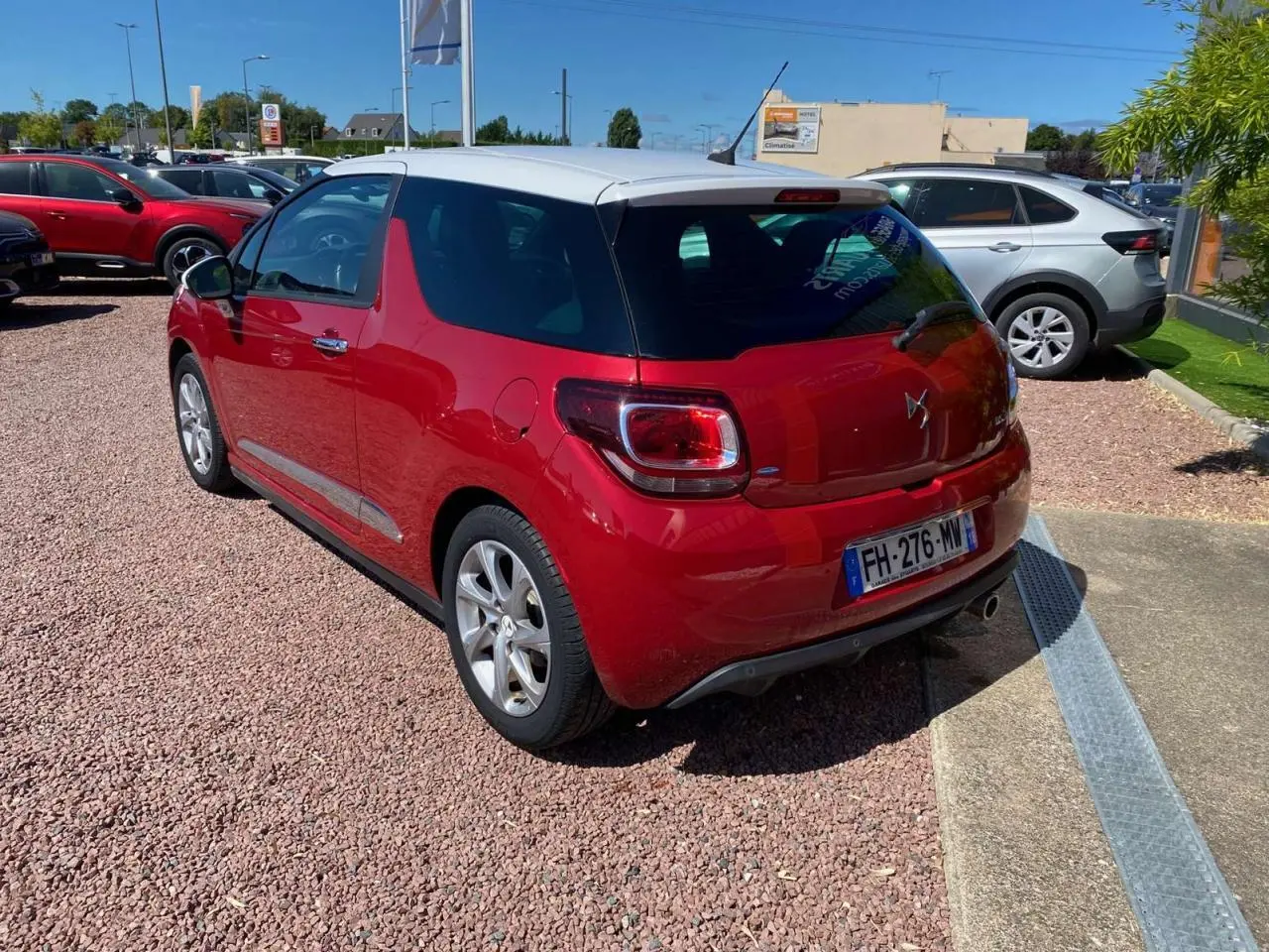Vue 3/4 arrière droite d'une DS3 rouge à toit blanc, avec jantes alliage et plaque d'immatriculation française.
