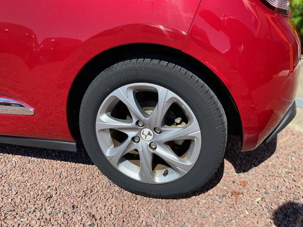 Gros plan sur la roue arrière droite argentée d'une DS3 rouge avec toit blanc, soulignant le design de la jante alliage.