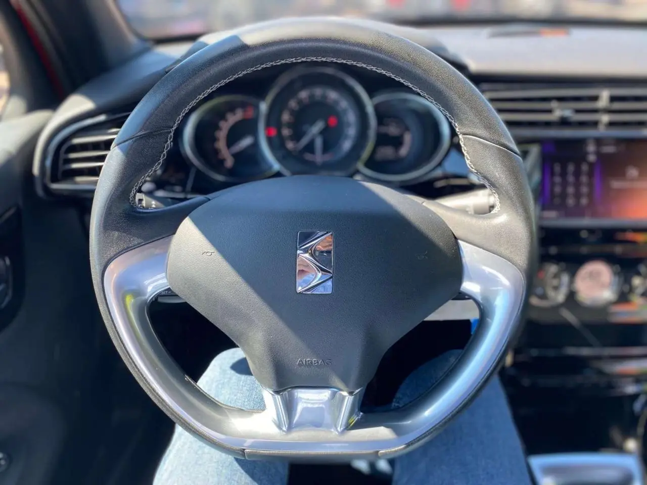 Vue rapprochée du volant DS3 2018 avec logo DS, tableau de bord et écran tactile en arrière-plan flou.