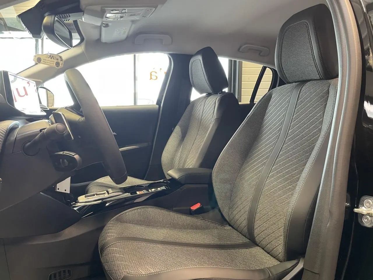 Vue intérieure côté conducteur de la Peugeot 208 noire 2025, sièges tissu gris avec surpiqûres Quartz et volant cuir.