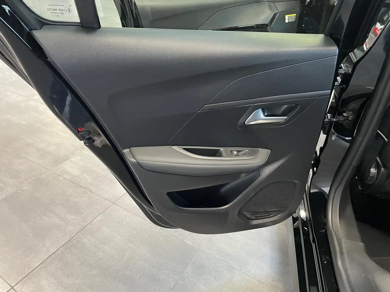 Vue intérieure de la porte arrière gauche noire du Peugeot 208 1.2i Hybrid Allure avec accoudoir gris clair et haut-parleur intégré.