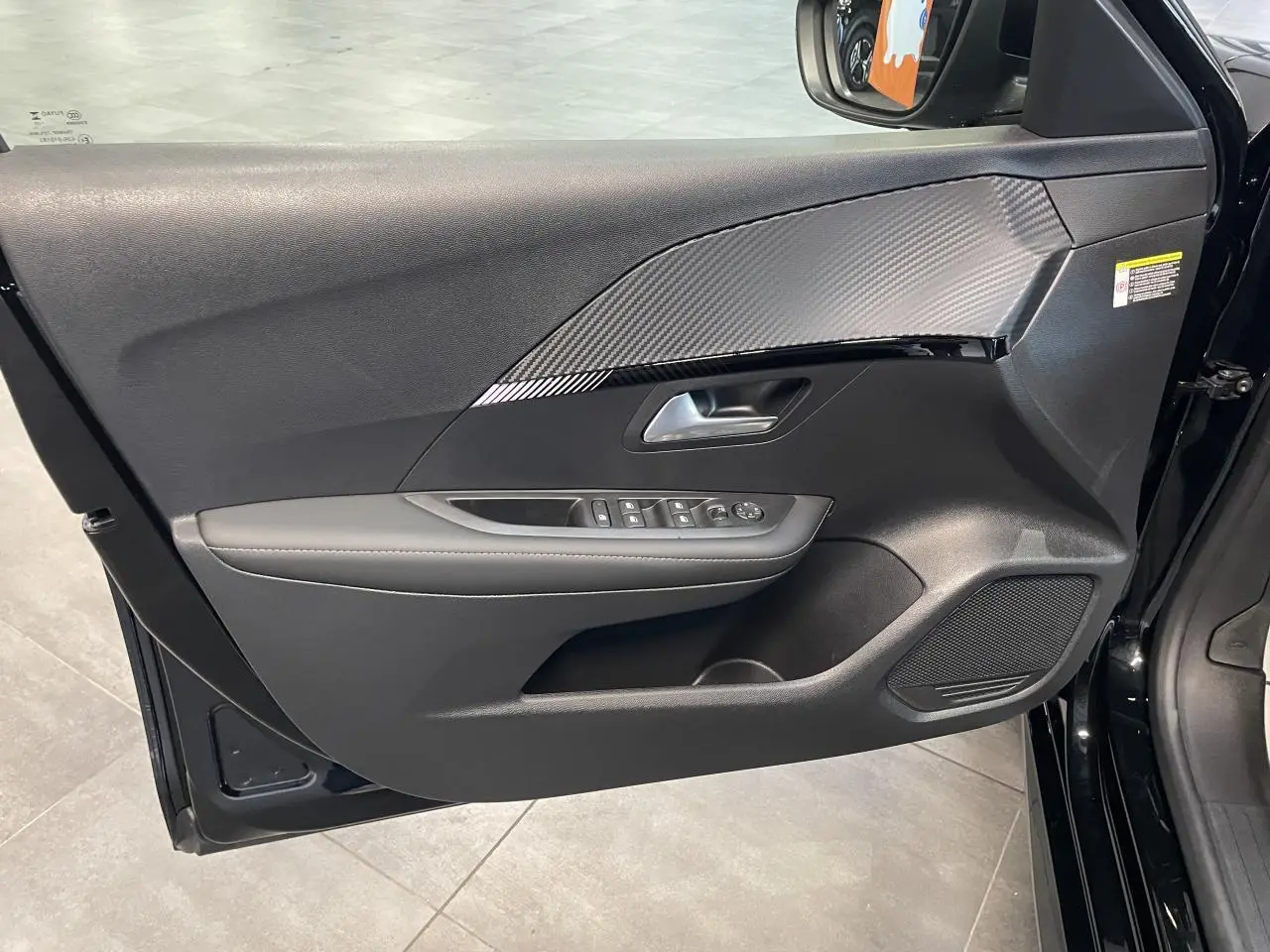 Vue intérieure côté gauche de la porte avant noire du Peugeot 208 Allure avec insert carbone et commandes électriques.