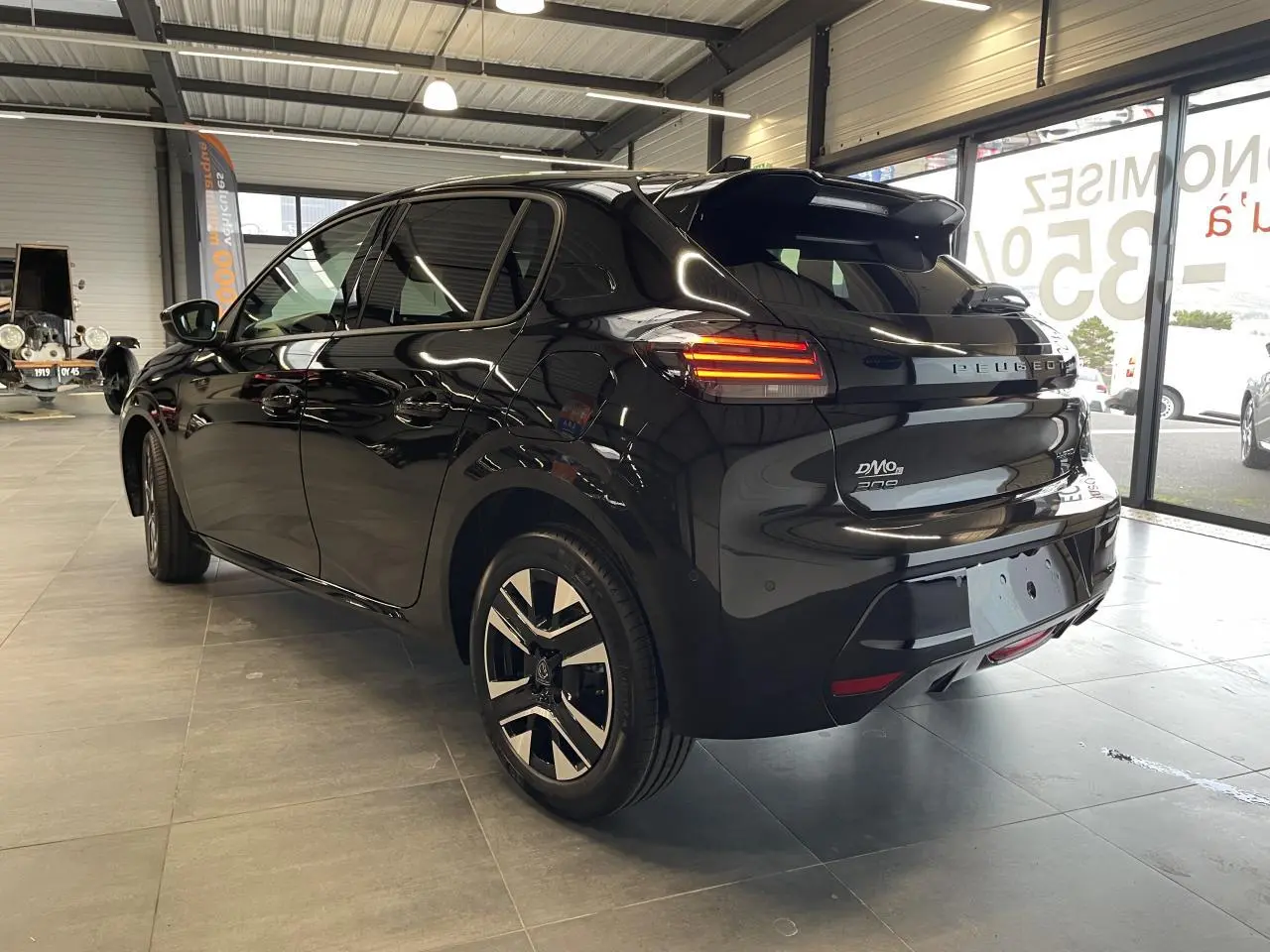 Peugeot 208 noire vue en 3/4 arrière droit dans un showroom, avec feux arrière LED allumés et jantes alliage.