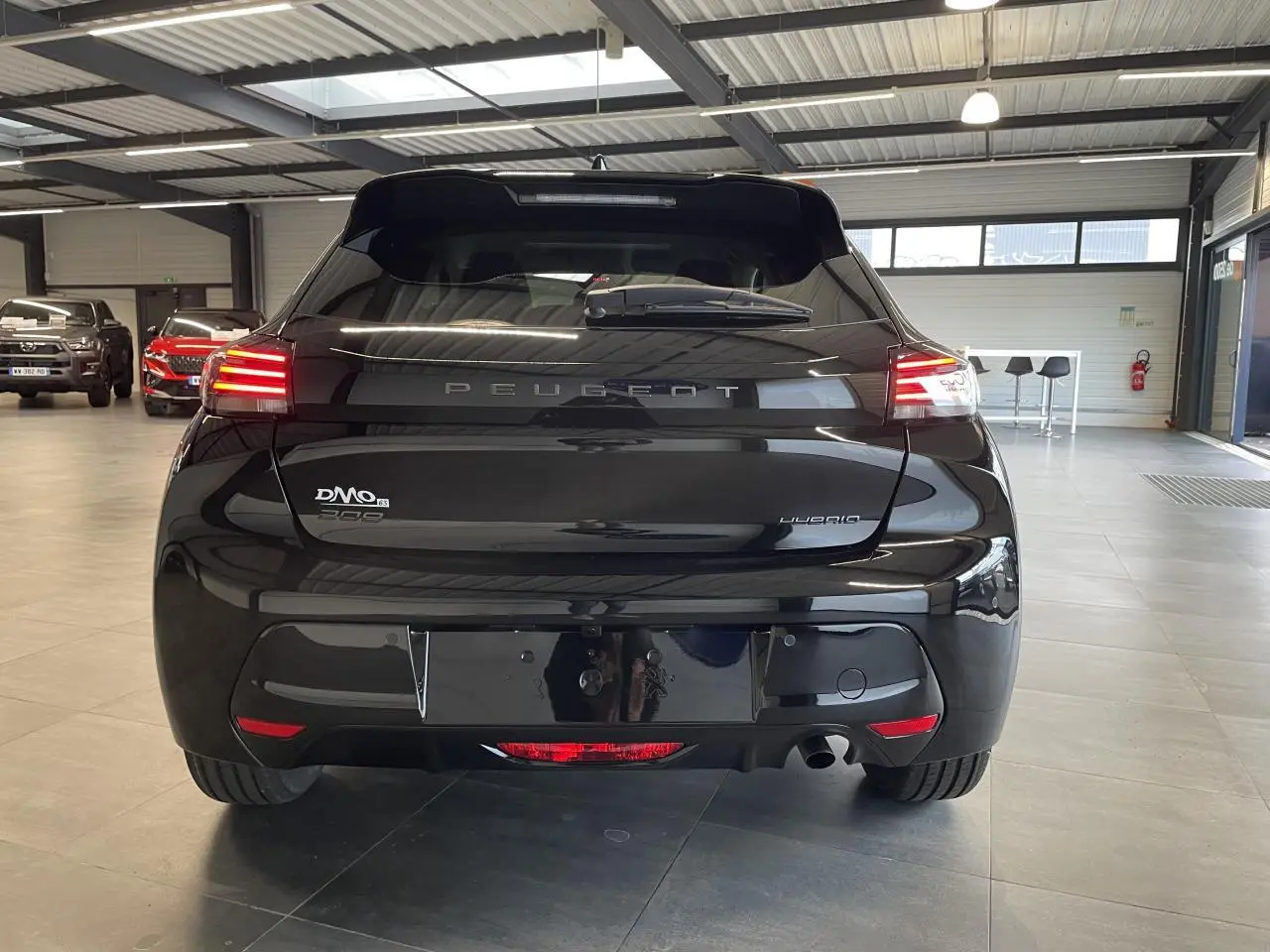 Vue arrière d'une Peugeot 208 noire avec feux arrière à LED et becquet noir brillant dans un garage.