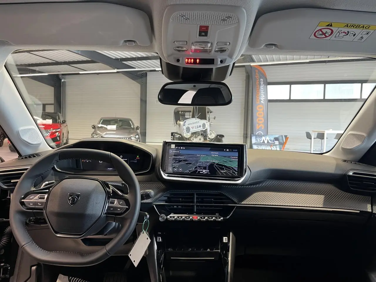 Vue intérieure avant du Peugeot 208 2025, tableau de bord noir avec écran tactile central et volant compact cuir.