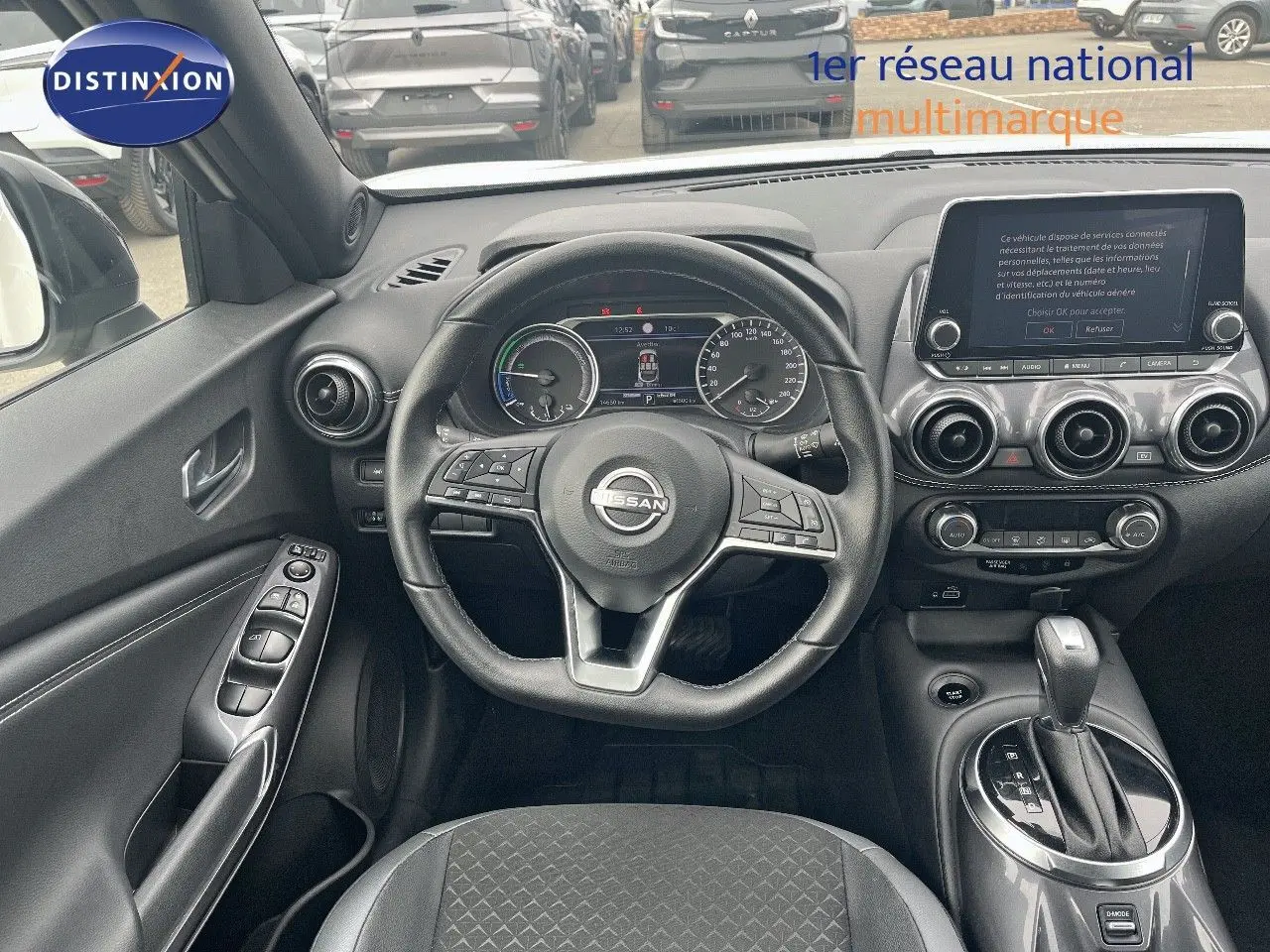 Vue intérieure centrée sur le poste de conduite du Nissan Juke 2024, volant cuir noir et console avec écran tactile.