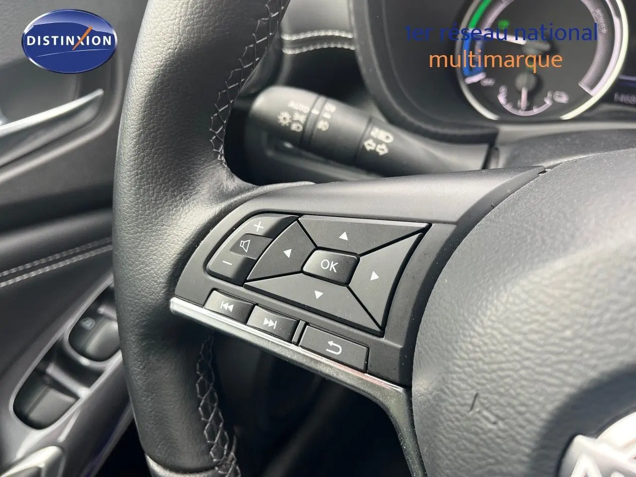 Gros plan sur les commandes multifonctions noires du volant du Nissan Juke blanc nacré 2024, avec tableau de bord en arrière-plan.