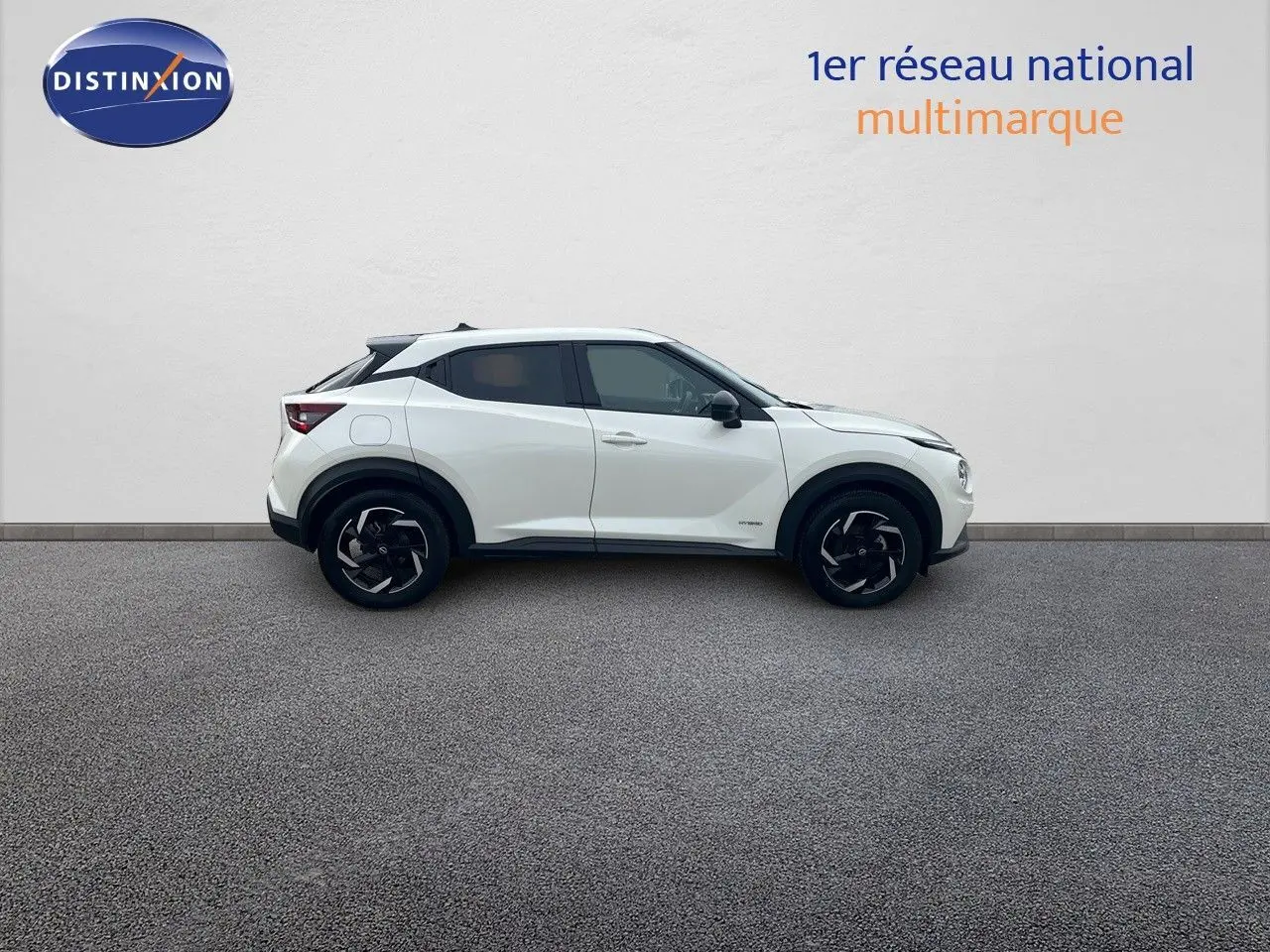 Vue de profil côté gauche d'un Nissan Juke blanc nacré 2024 avec jantes noires et toit contrasté noir.