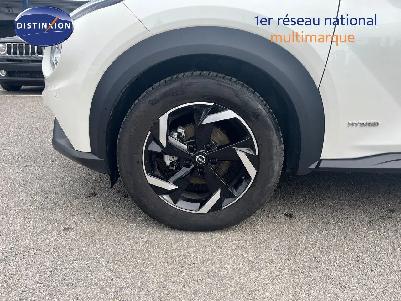 Gros plan sur la roue avant droite et la partie latérale blanche nacrée du Nissan Juke 1.6 HEV 143ch avec badge Hybrid visible.