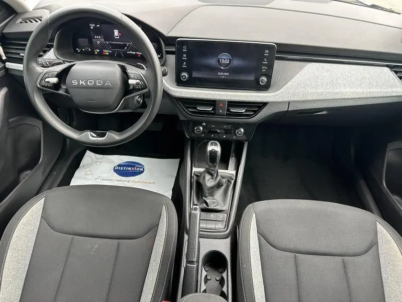 Vue intérieure avant de la Skoda Scala 2025, tableau de bord moderne avec écran tactile et sièges tissu noir/gris.