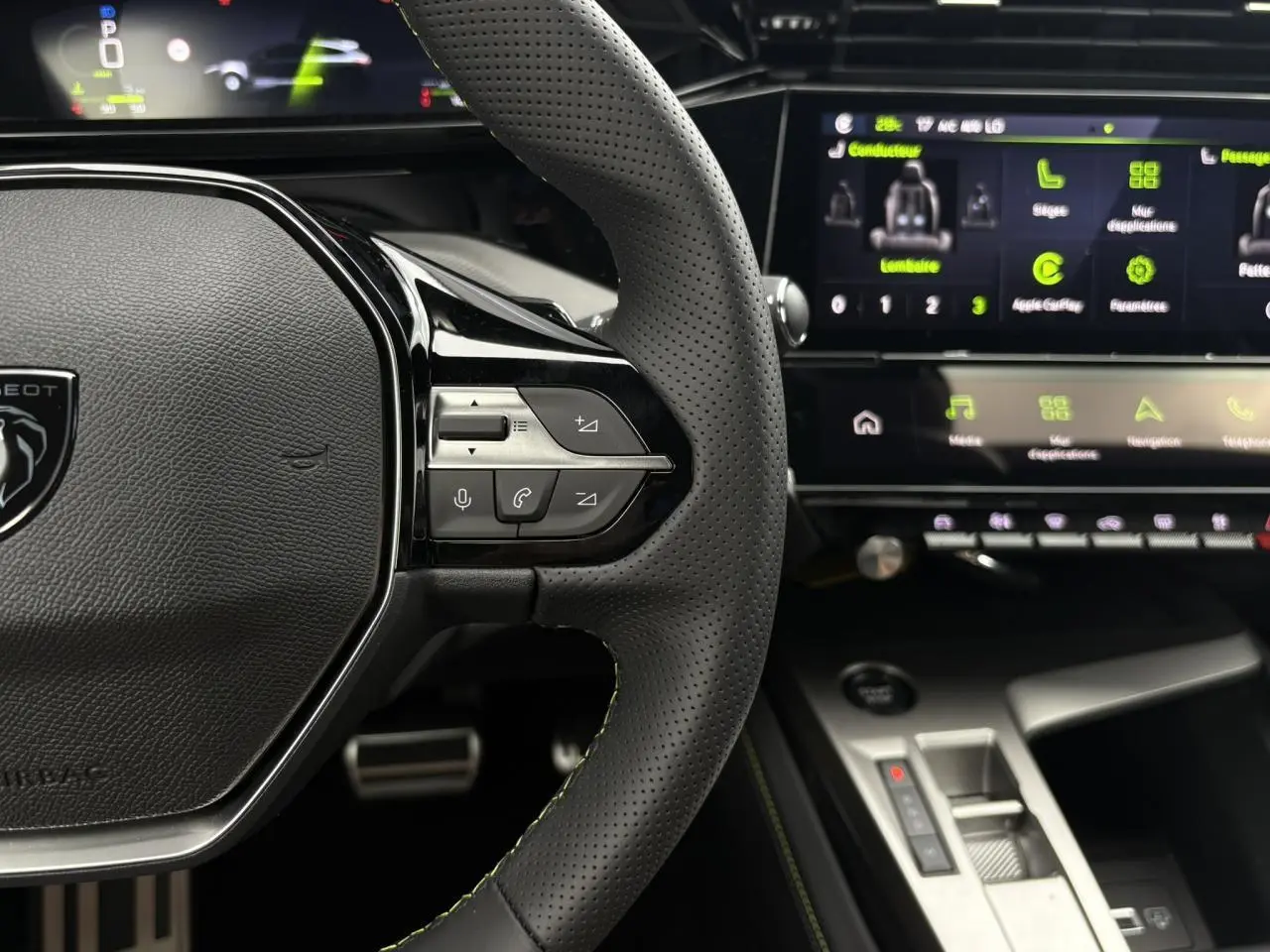 Vue rapprochée du volant perforé noir avec surpiqûres vert Adamite et écran tactile du Peugeot 308 SW Hybrid 2026.