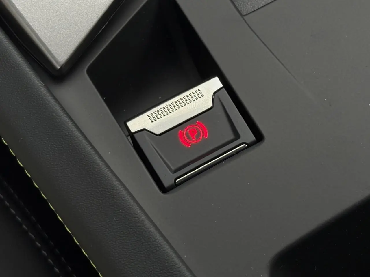 Gros plan sur le bouton de frein de parking électrique illuminé en rouge dans l'habitacle noir de la Peugeot 308 SW 2026.