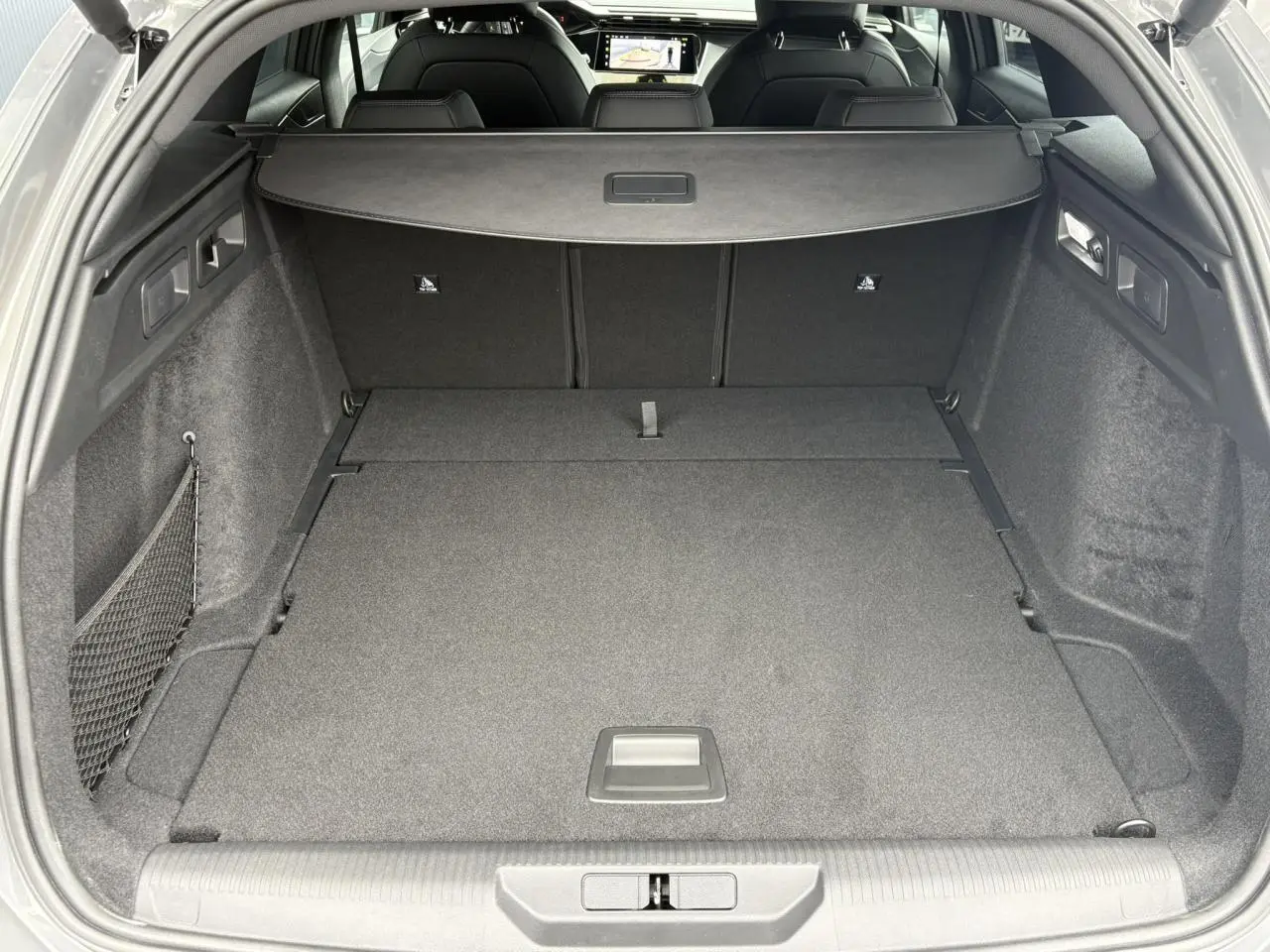 Coffre ouvert d’une Peugeot 308 SW gris Sélénium, vue arrière montrant un espace de chargement plat et un filet latéral.