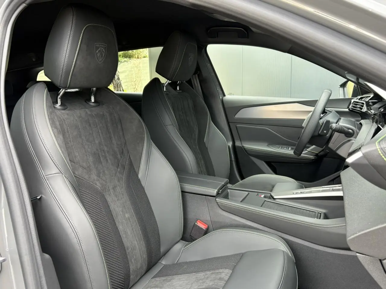 Vue intérieure côté conducteur de la Peugeot 308 SW 2026, sièges Alcantara noirs avec surpiqûres vert Adamite et volant compact cuir.
