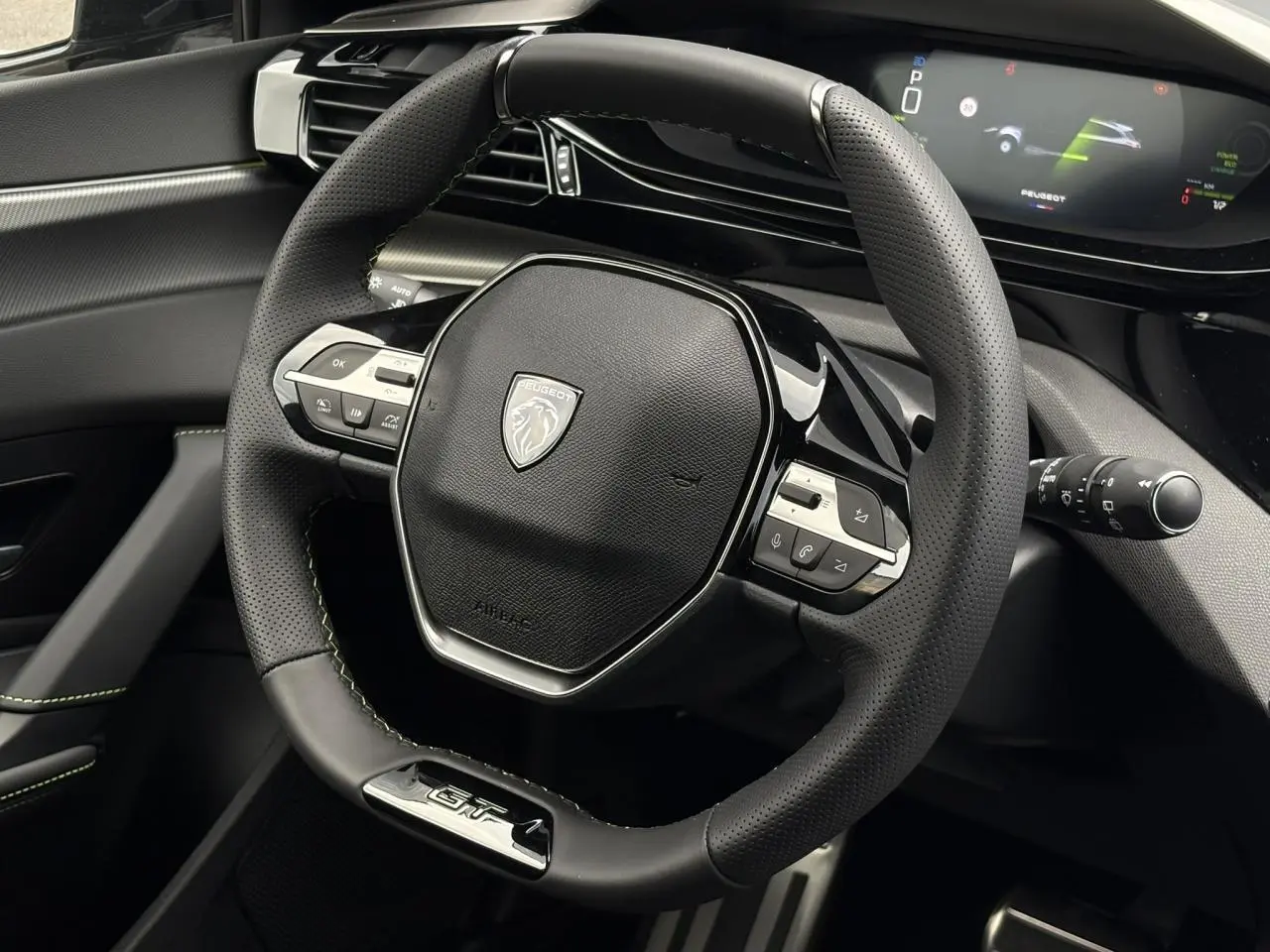 Vue rapprochée du volant GT en cuir noir avec surpiqûres vertes et combiné numérique du Peugeot 308 SW 2026.