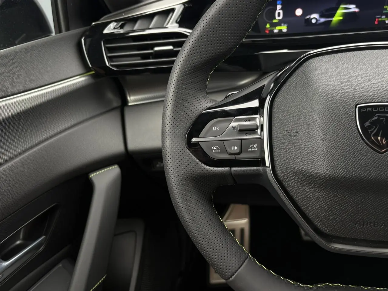 Gros plan sur le volant perforé noir avec surpiqûres vert Adamite et partie gauche du tableau de bord gris et noir du Peugeot 308 SW Hybrid.