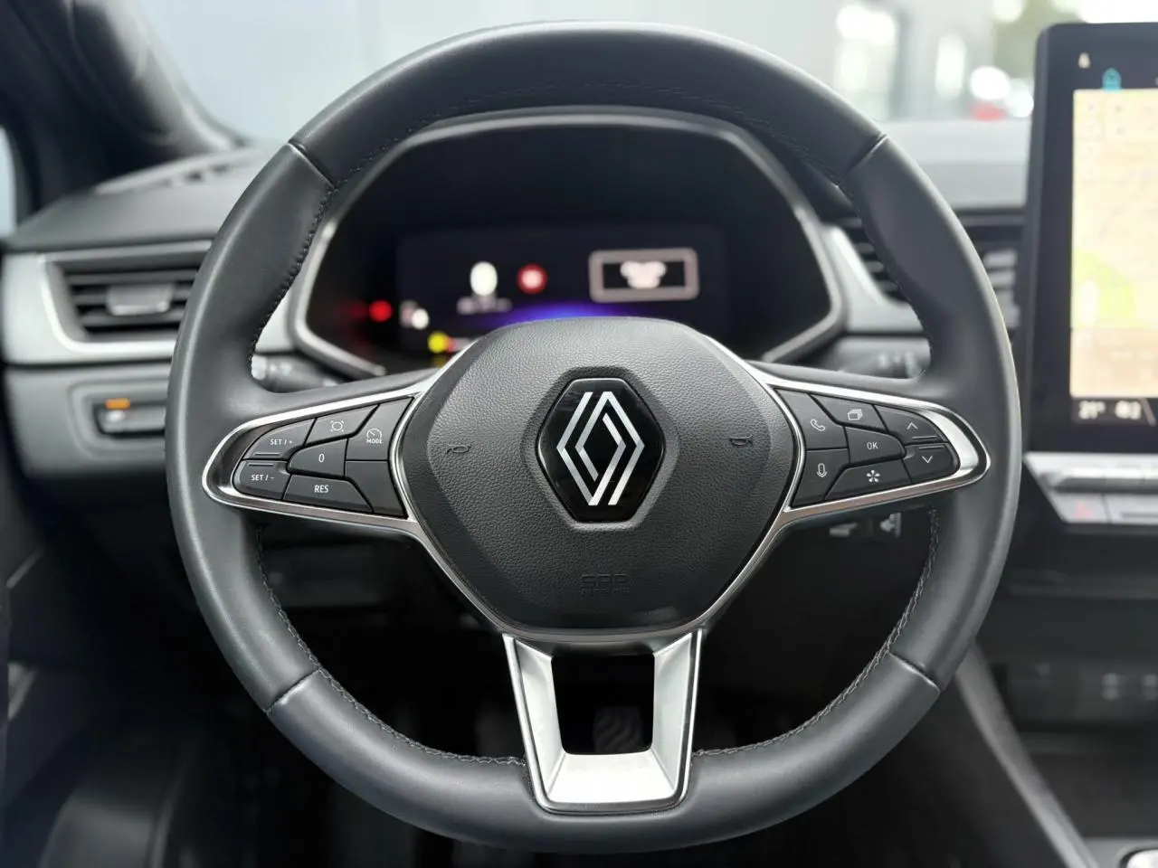 Vue rapprochée du volant noir du Renault Captur TCE 100 Techno 2025 avec commandes intégrées et tableau de bord numérique flou.