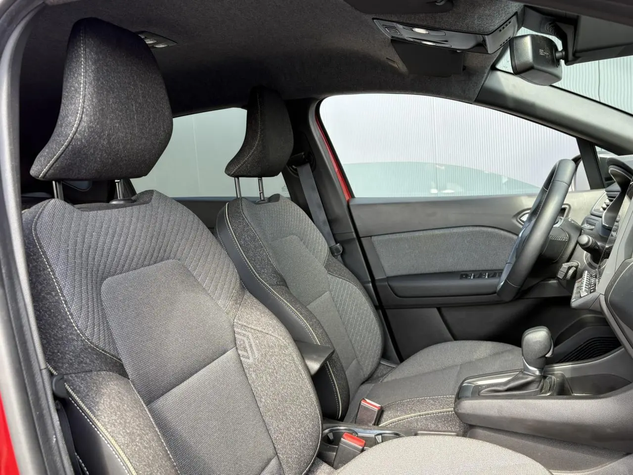 Vue intérieure côté gauche du Renault Captur E-Tech rouge, montrant les sièges avant en tissu gris et la console centrale.