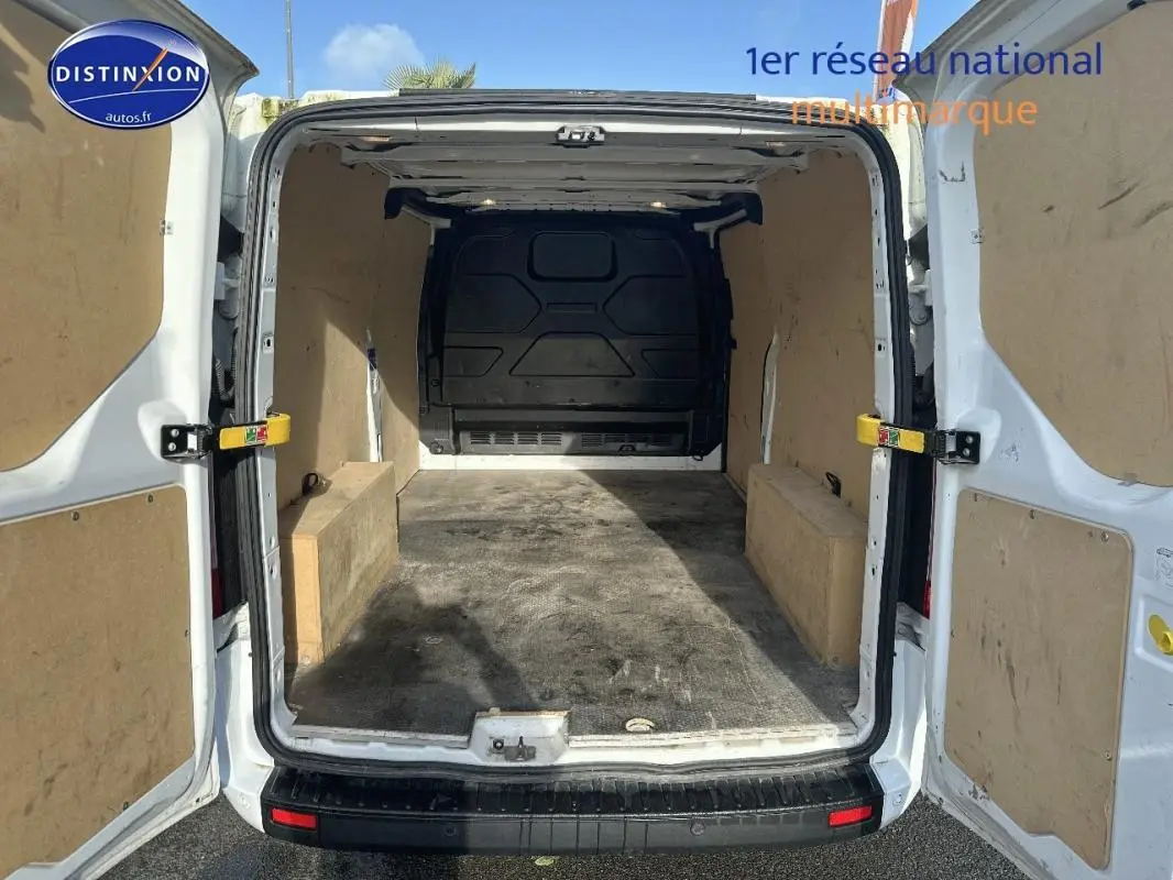 Vue arrière du fourgon blanc Ford Transit Custom avec portes ouvertes montrant l’espace de chargement vide et protégé.