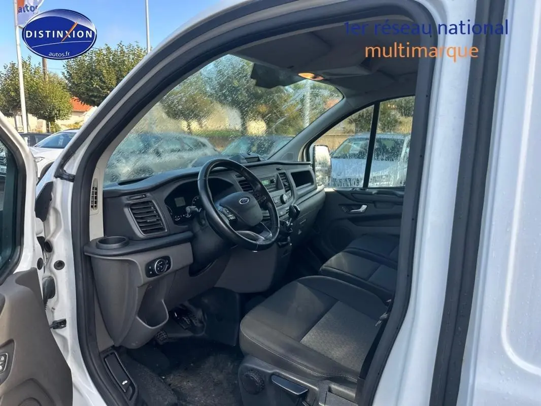 Vue intérieure côté conducteur du Ford Transit Custom blanc de 2021, montrant le tableau de bord et les sièges noirs.