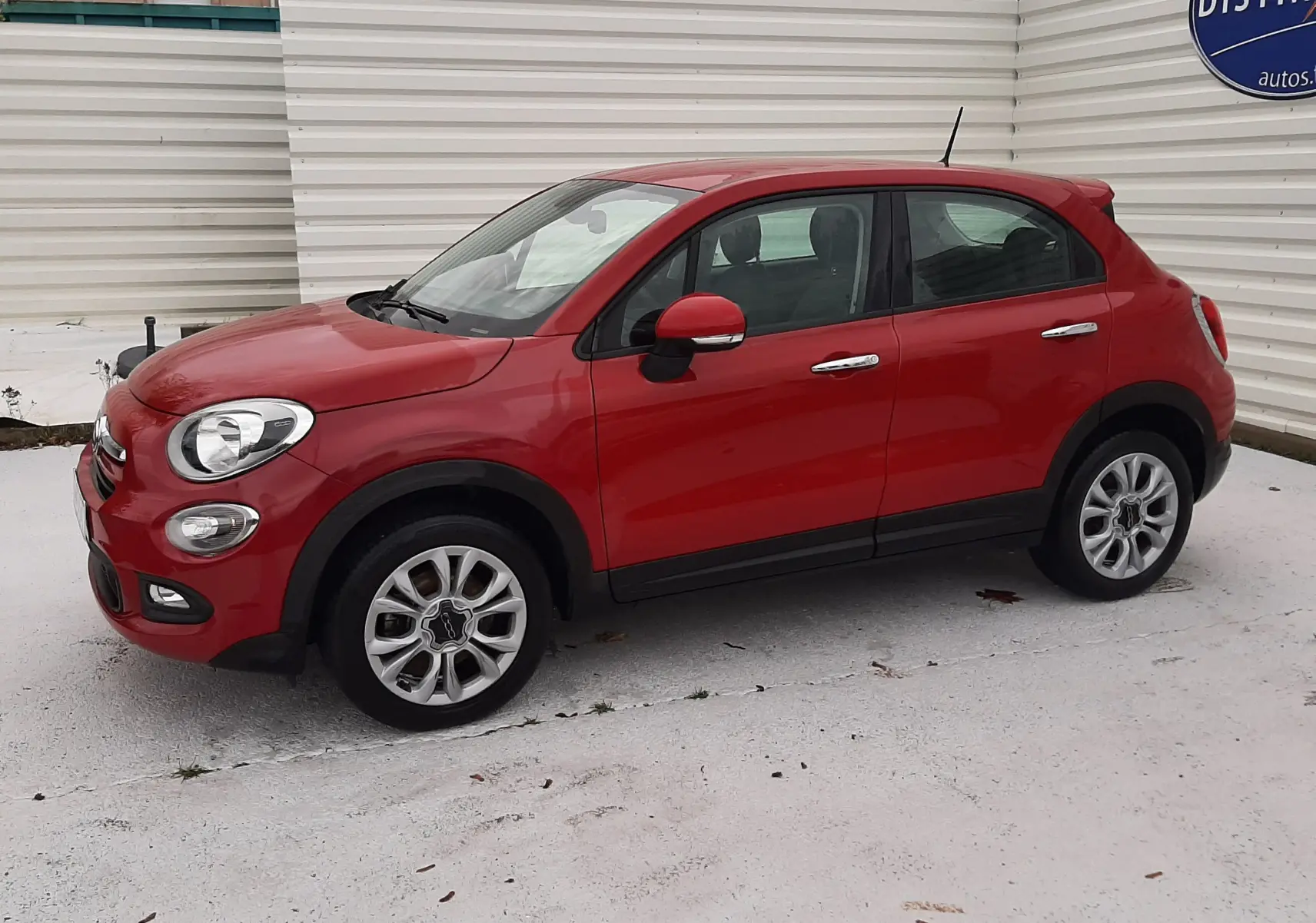 Vue 3/4 avant droit d'une FIAT 500X rouge avec rétroviseur et poignées chromées sur fond clair.