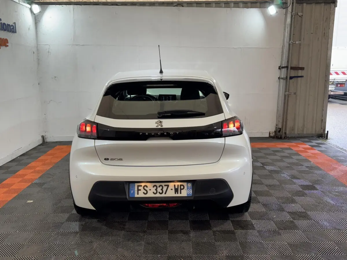 Vue arrière d'une Peugeot 208 électrique Active Business blanche, avec feux arrière allumés et plaque d'immatriculation visible.