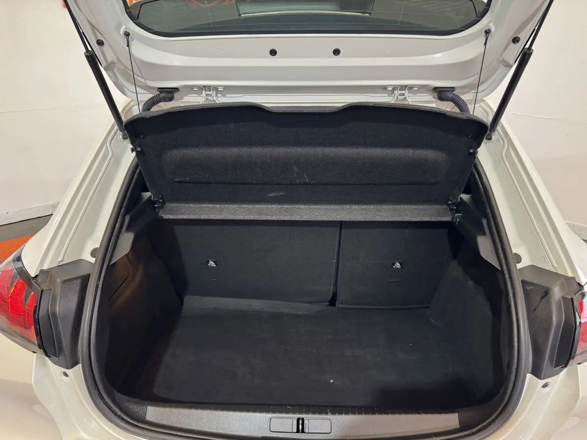 Coffre ouvert vu de l'arrière d'une Peugeot 208 Electrique Active Business blanche, intérieur noir et banquette rabattable.