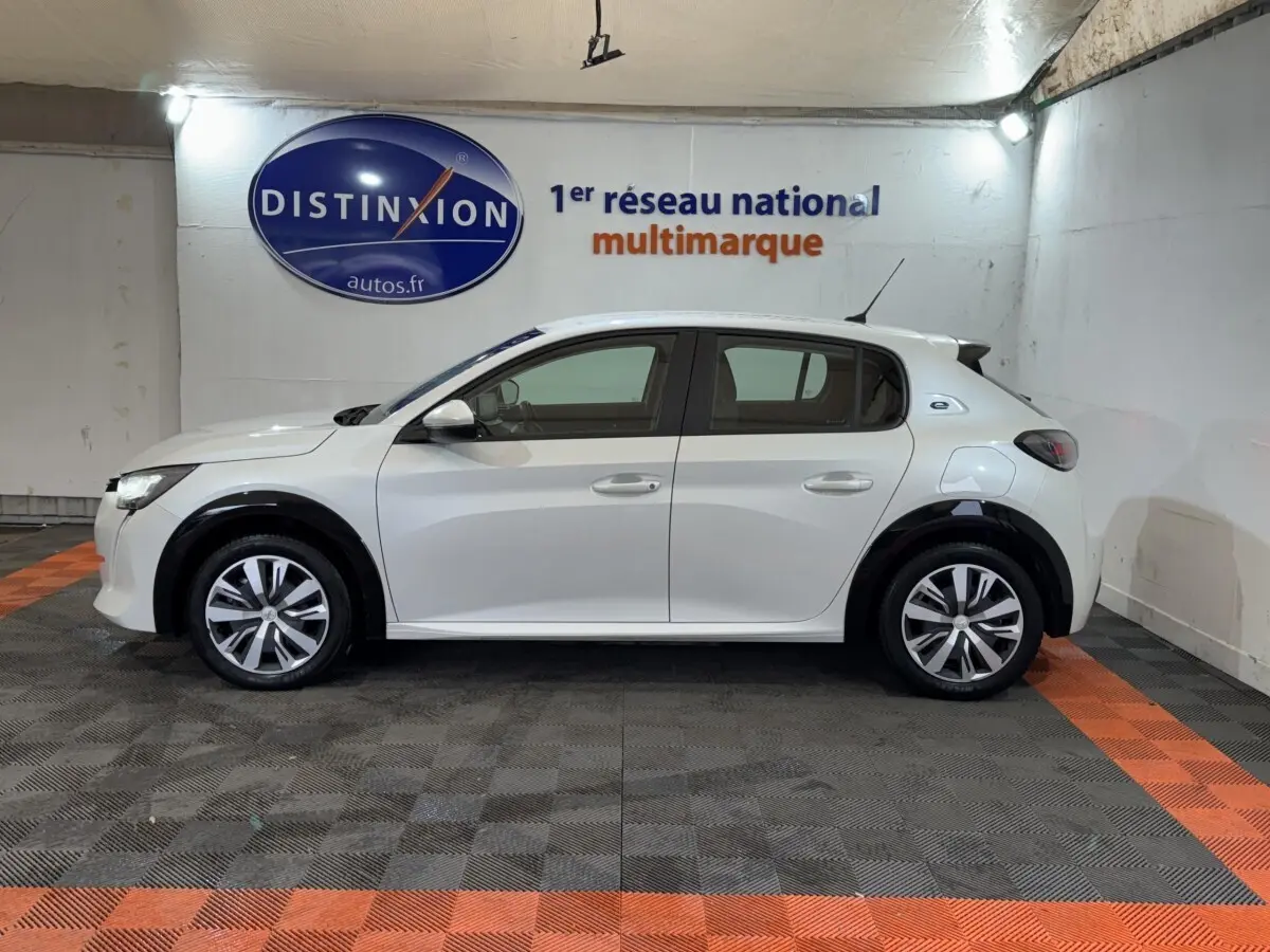 Peugeot 208 Electrique Active Business vue de profil côté gauche, couleur blanche, en intérieur sur sol damier noir et orange.