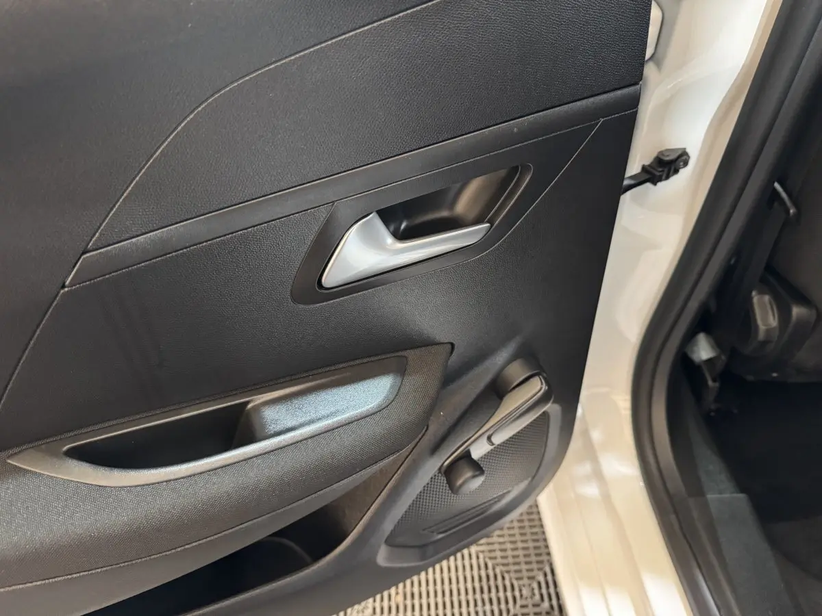 Vue rapprochée de la porte arrière droite noire avec poignée argentée et manivelle de vitre d'une Peugeot 208 électrique blanche.